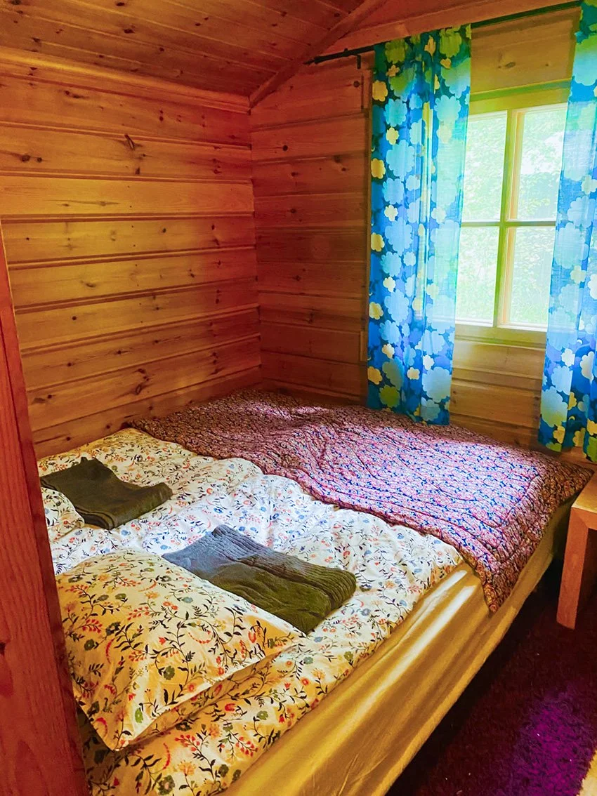 Puuseinäisessä huoneessa sänky kukallisilla lakanoilla.