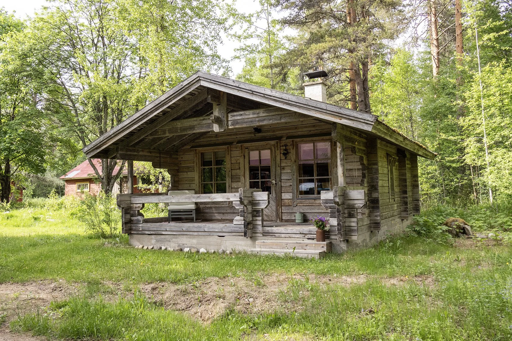 Harmaa puumökki vihreässä maisemassa.