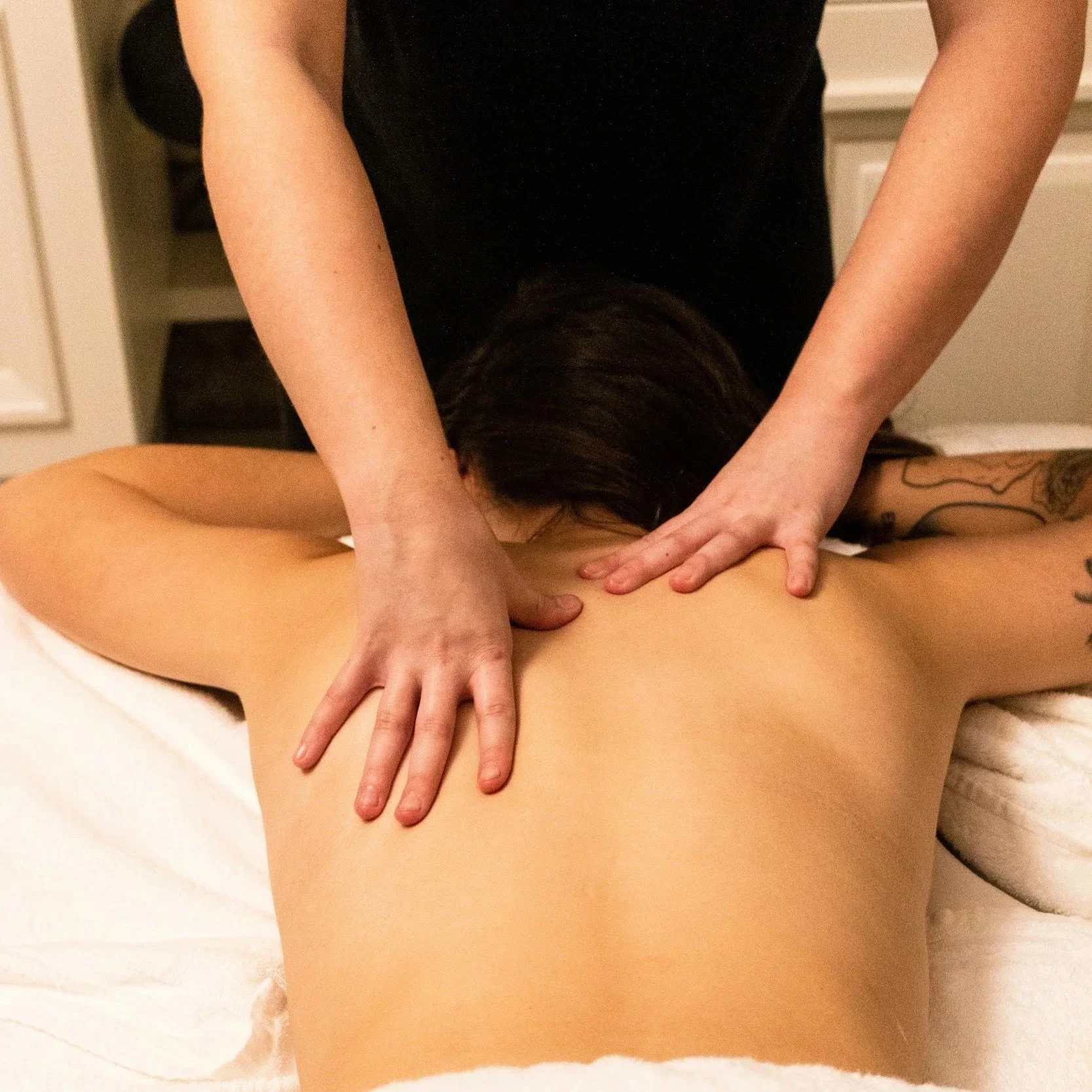 A person is receiving a massage on their back from a massage therapist in a room with a white cabinet in the background.