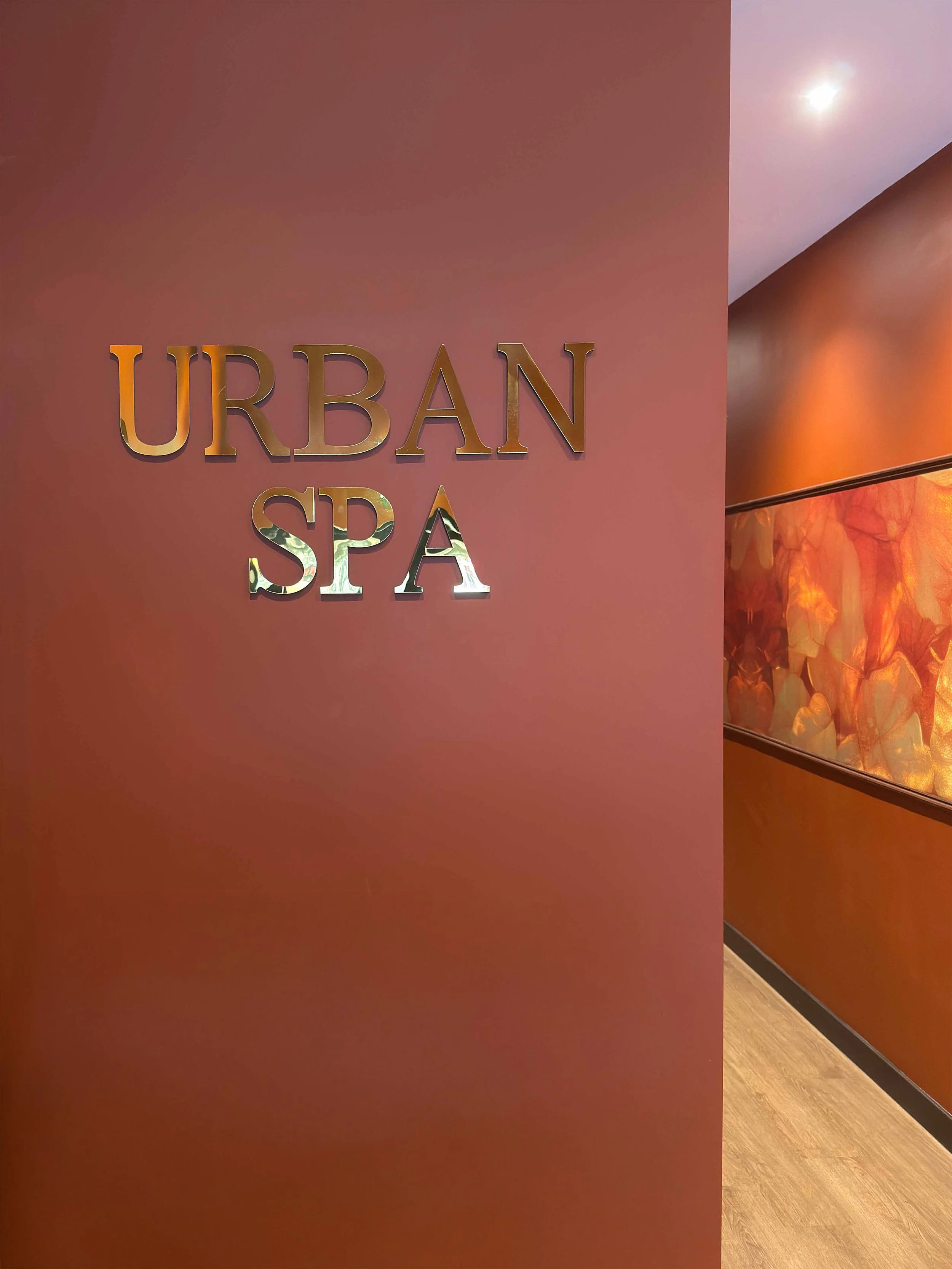 A wall with the words 'Urban Spa' in metallic letters, part of a hallway with warm lighting and decorative artwork.