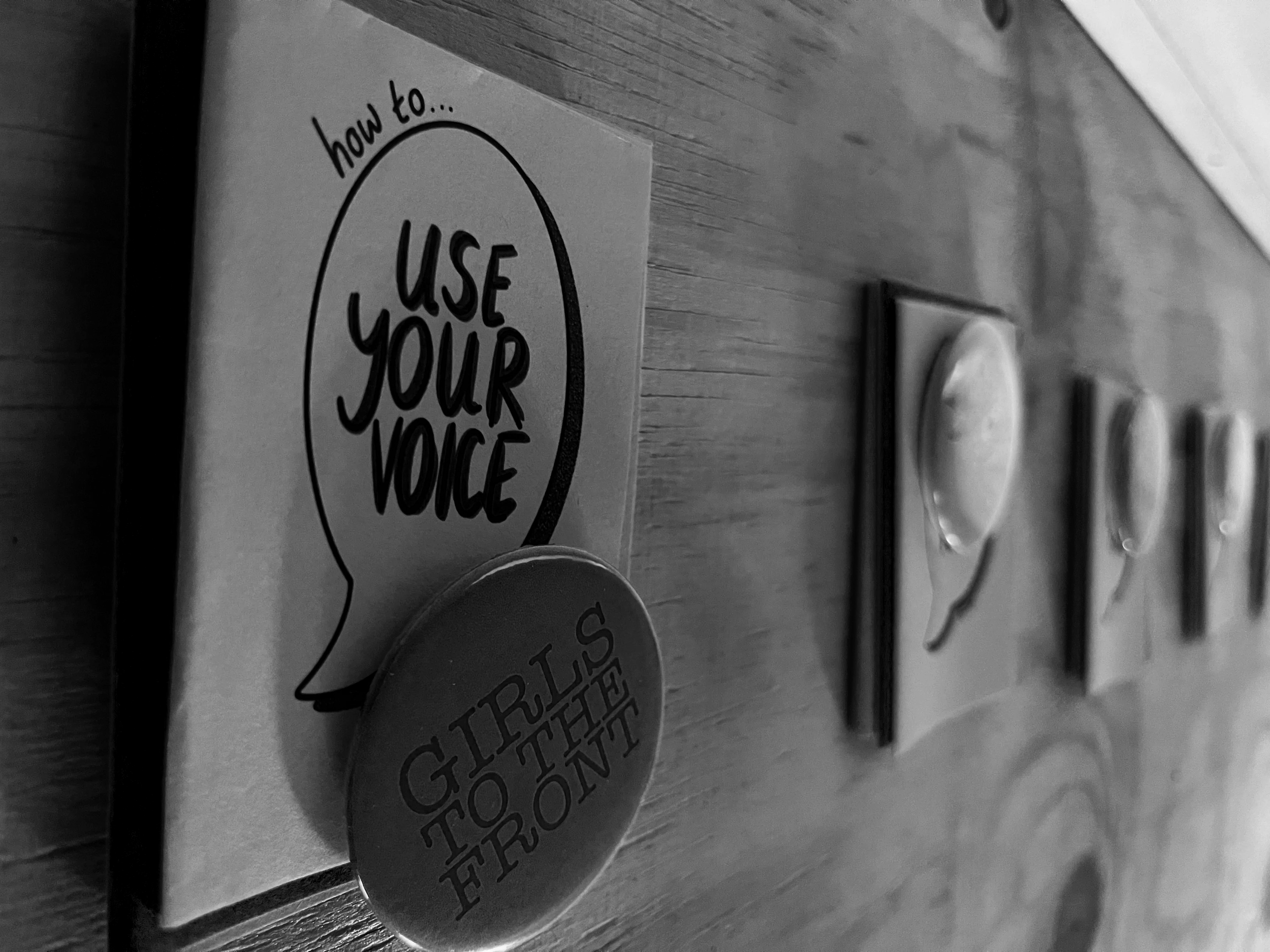 A wall with a motivational sign that says 'how to... USE YOUR VOICE' and a round button that says 'HURTS TO THE FRONT.'