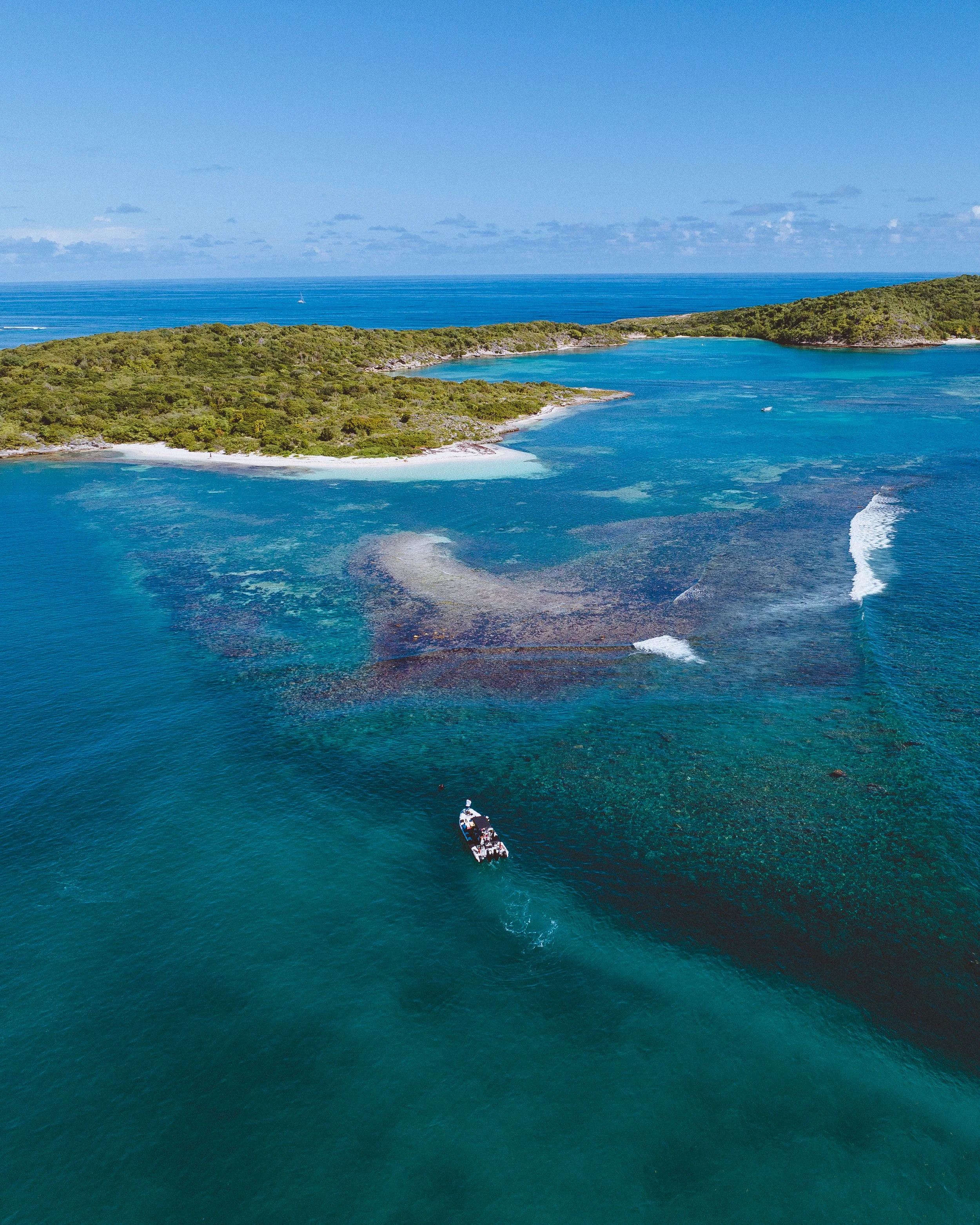 Aerial view of a boat in clear blue ocean near a green island with sandy beaches and shallow waters.