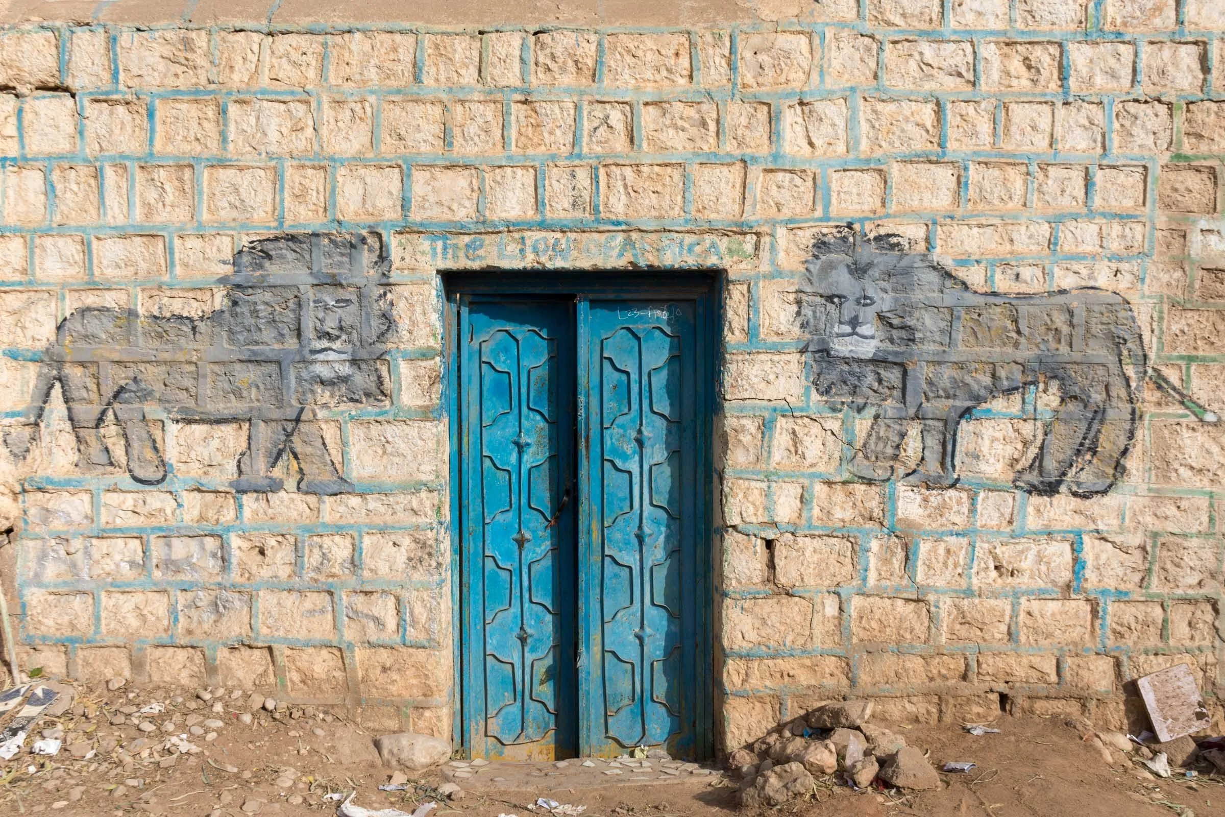 Two lions are painted on the exterior wall of a home around a blue door marked The Lions of Africa