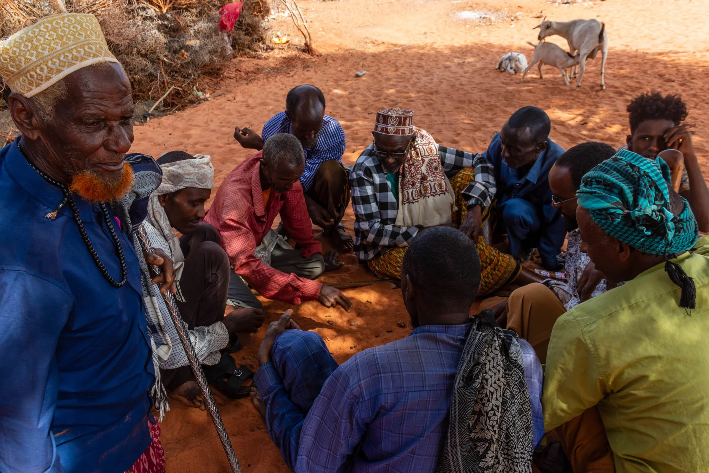 A group of men sit on the ground playing a game of shax