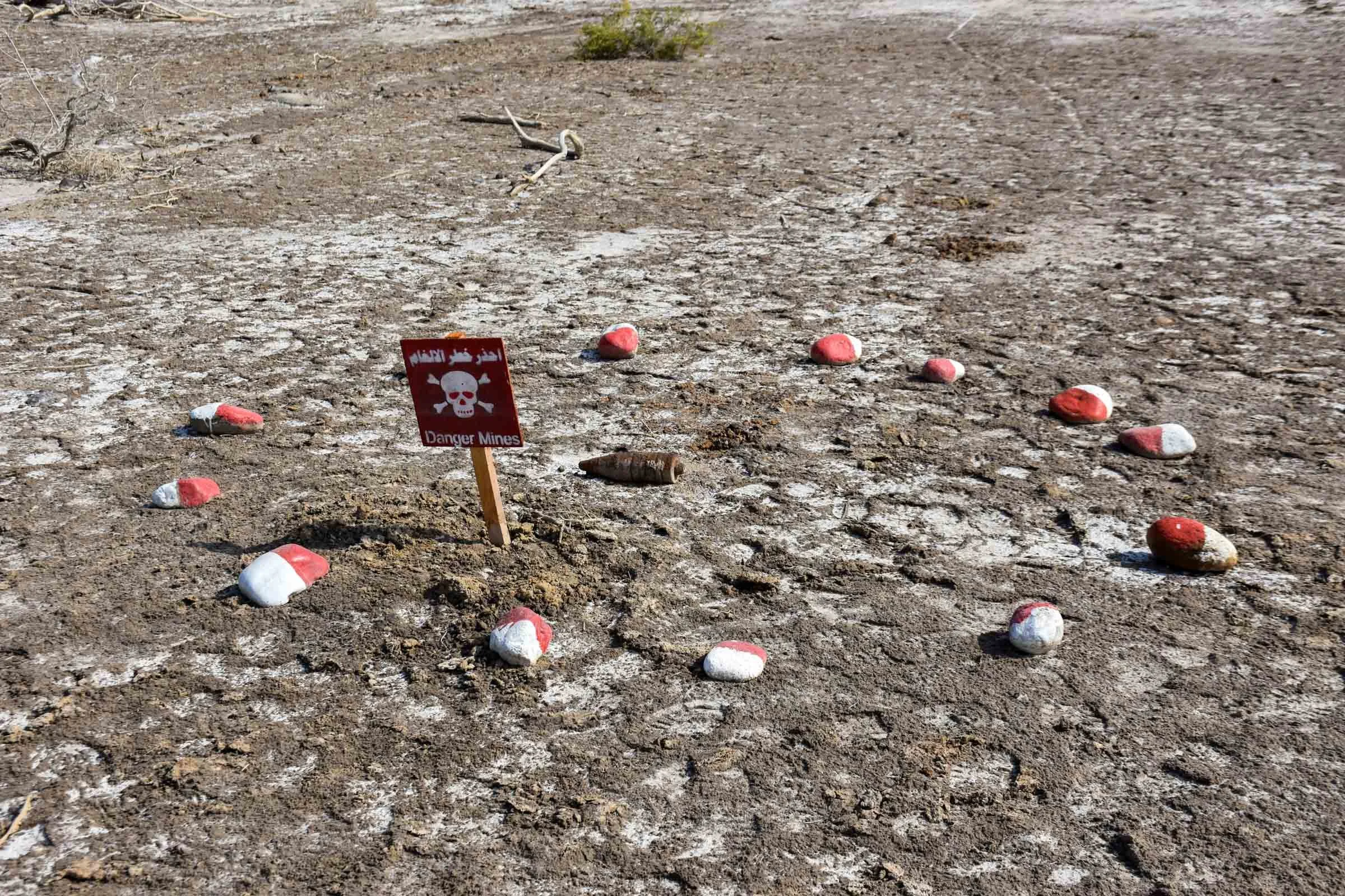 A circle of red and white painted stones and a danger sign surround a munition