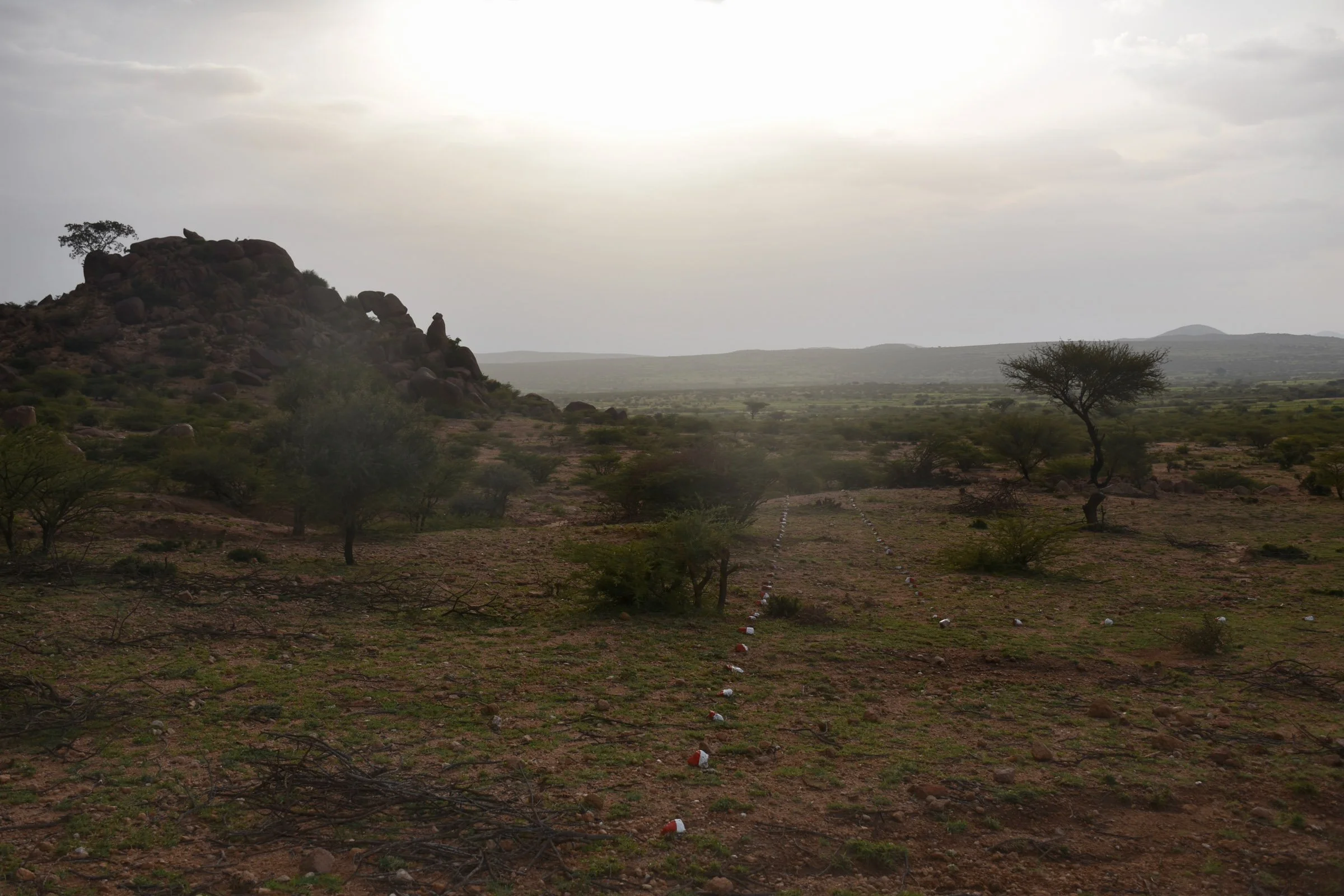 A line of red and white painted stones stretch into the distance underneath a landscape of boulders and crags