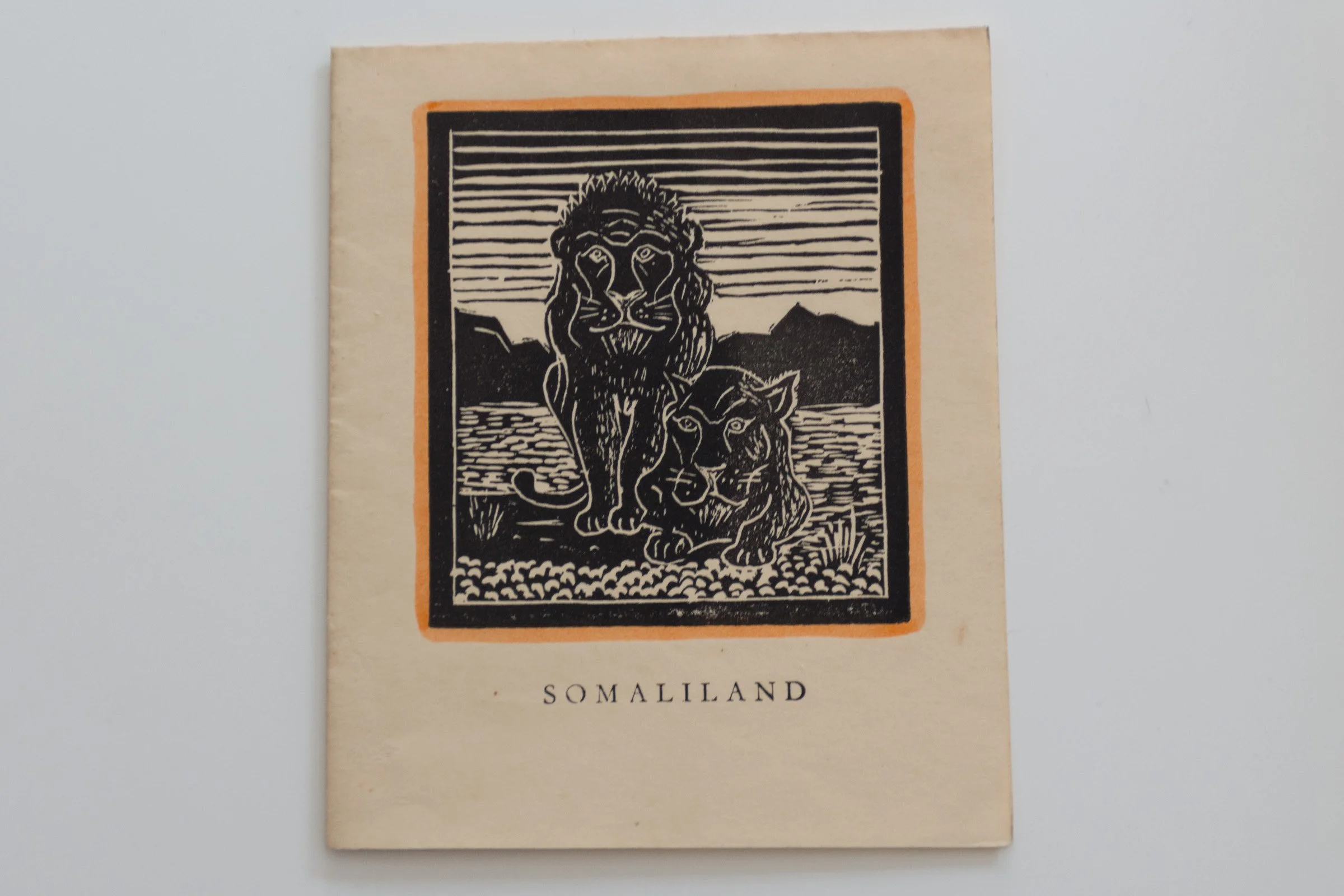 A printed card titled Somaliland shows a drawing of two lions against a mountainous and scrubby backdrop. Print by Kenneth Green, mid-20th century.