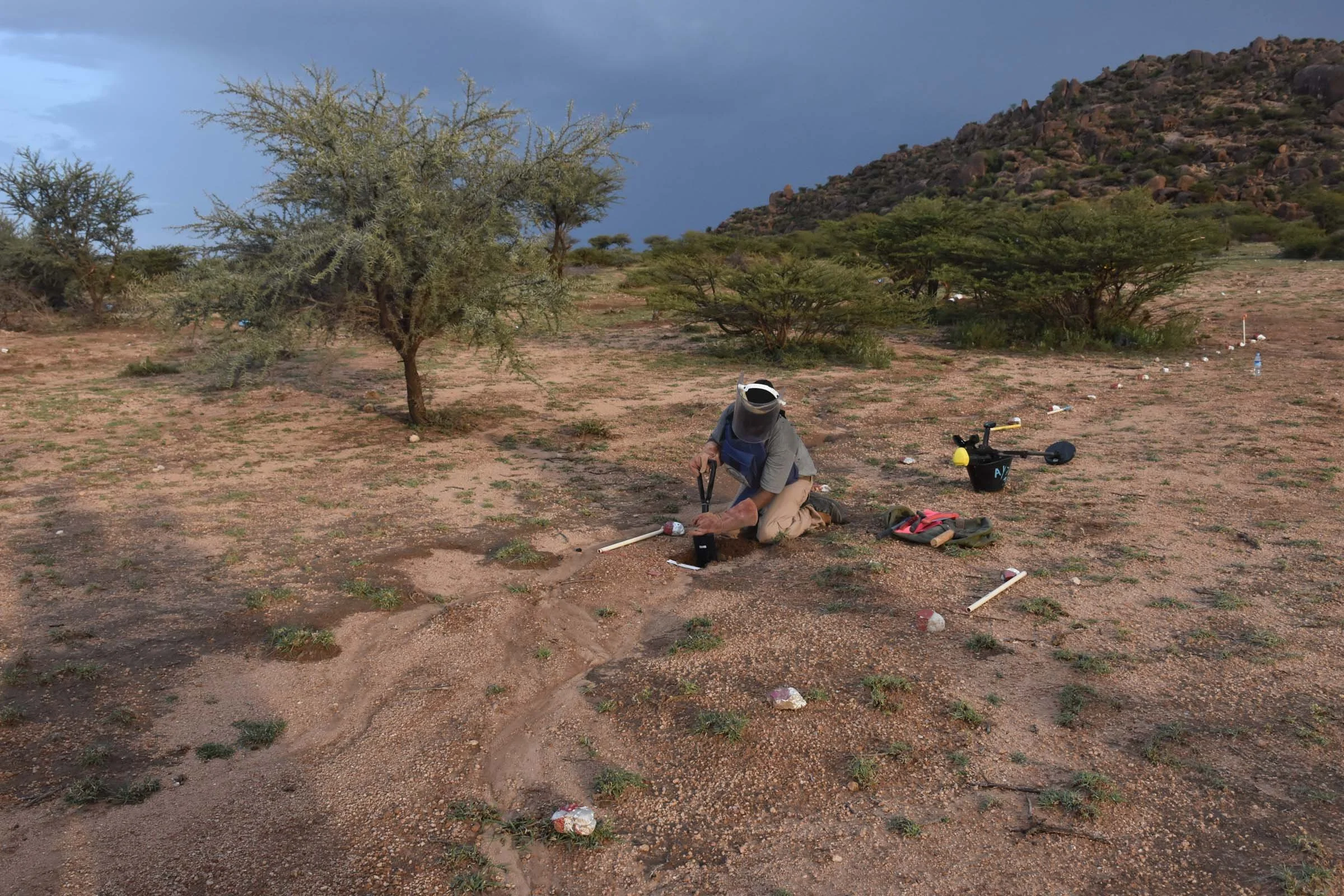 A man wearing personal protective equipment excavates earth in a minefield