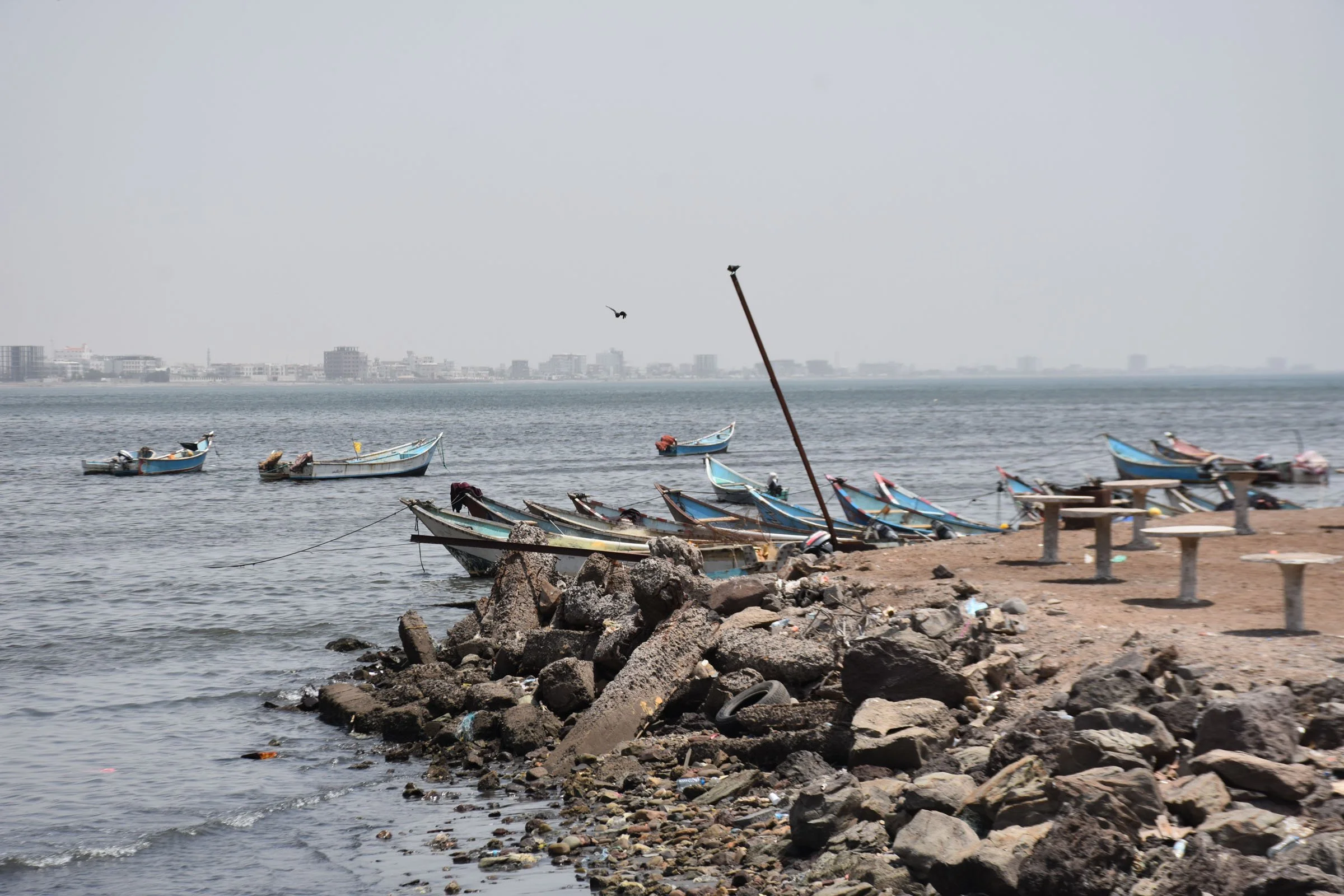 A view of small boats and empty tables in front of a cityscape