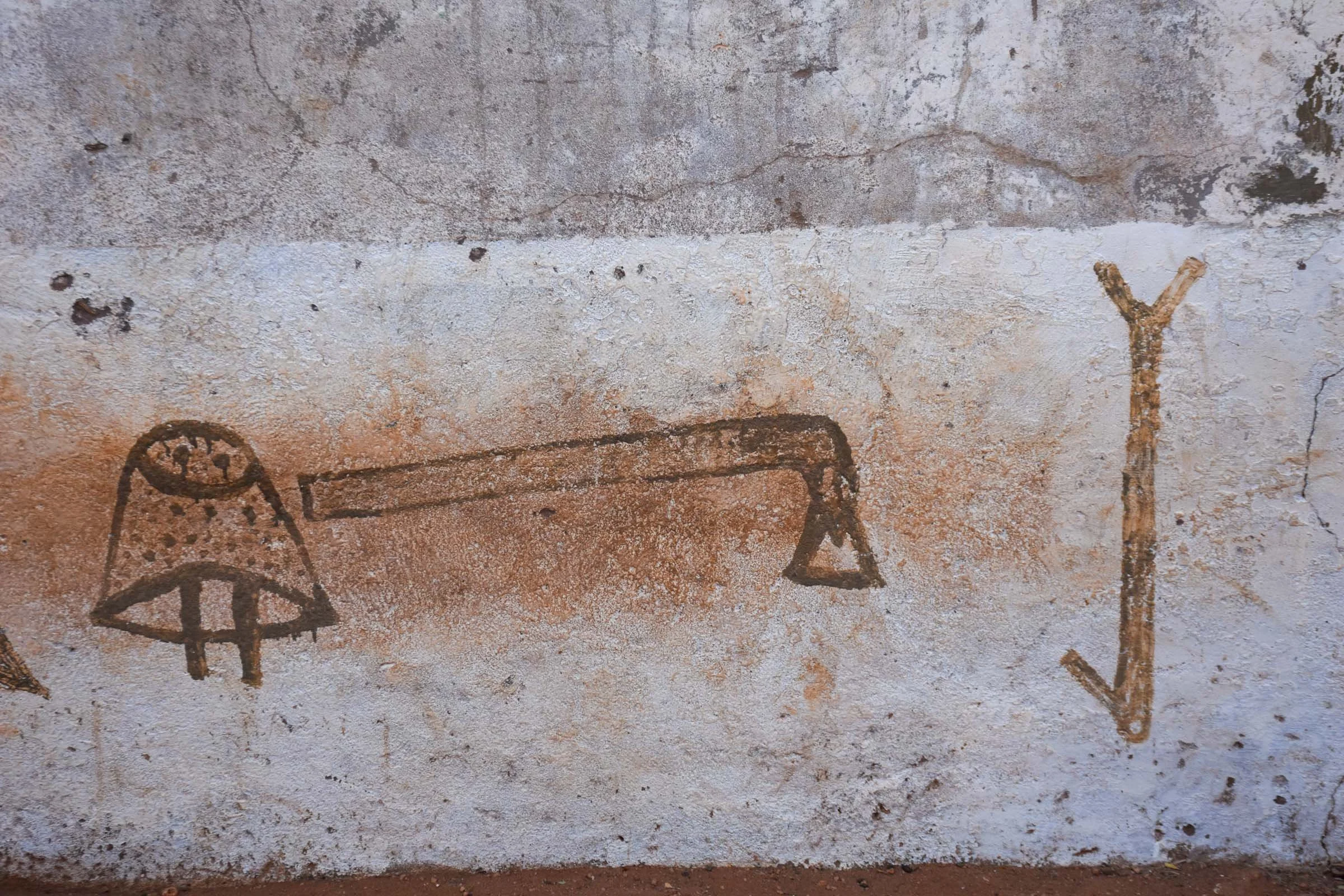 A white wall is painted with images of a shepherd’s stick, camel bell and axe