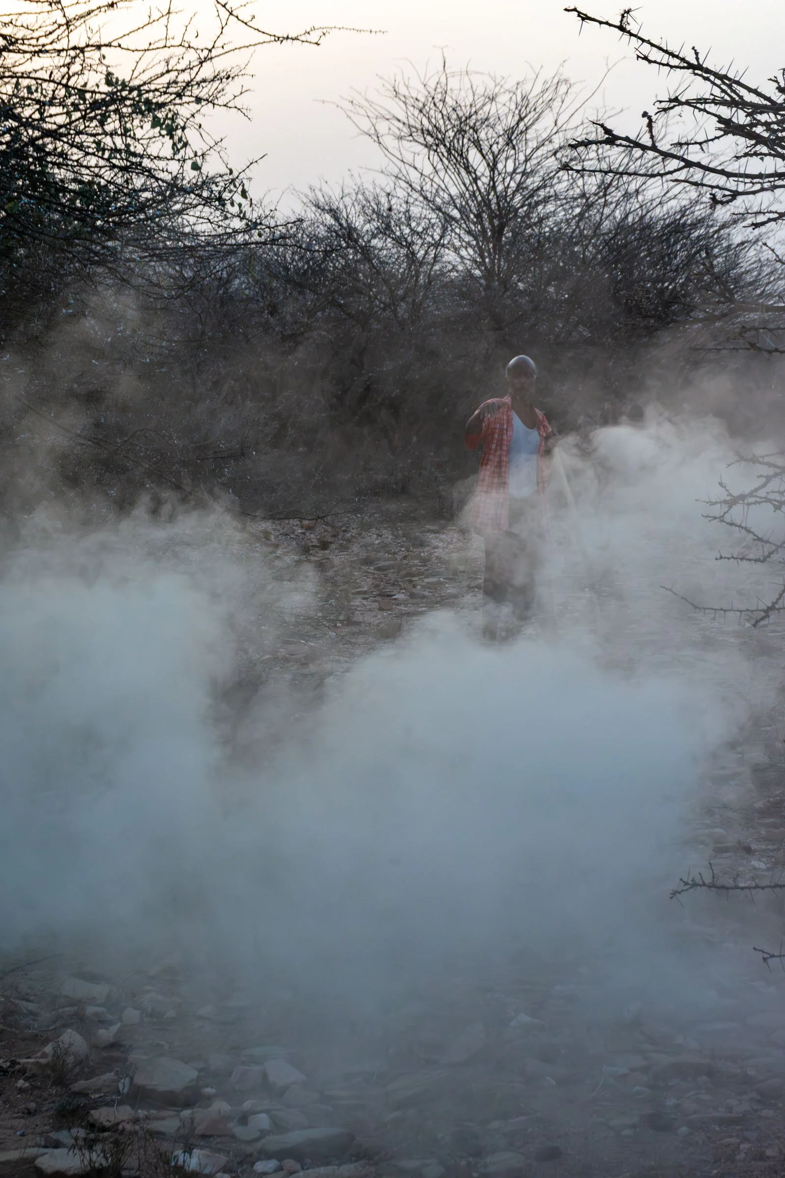 A man appears through smoke, surrounded by trees