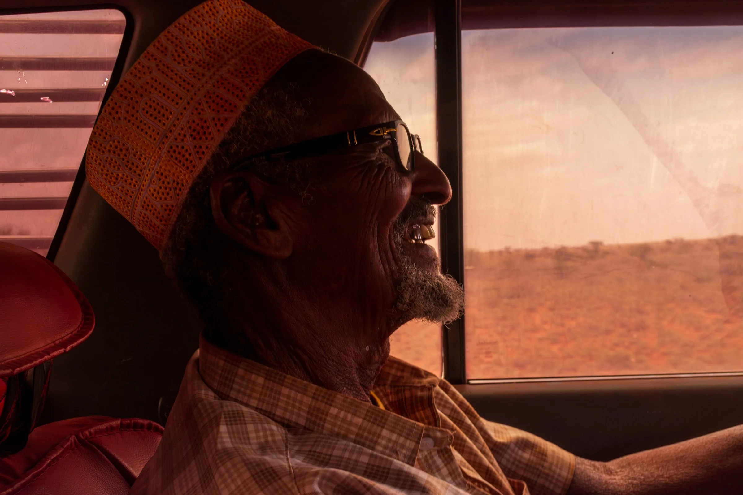 A man smiles inside a car with desert shown through the window