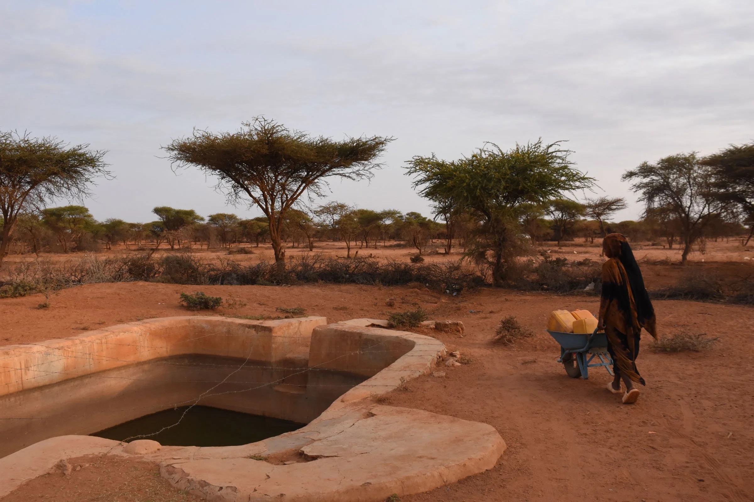A woman pushes a wheelbarrow in front of a burked water storage facility