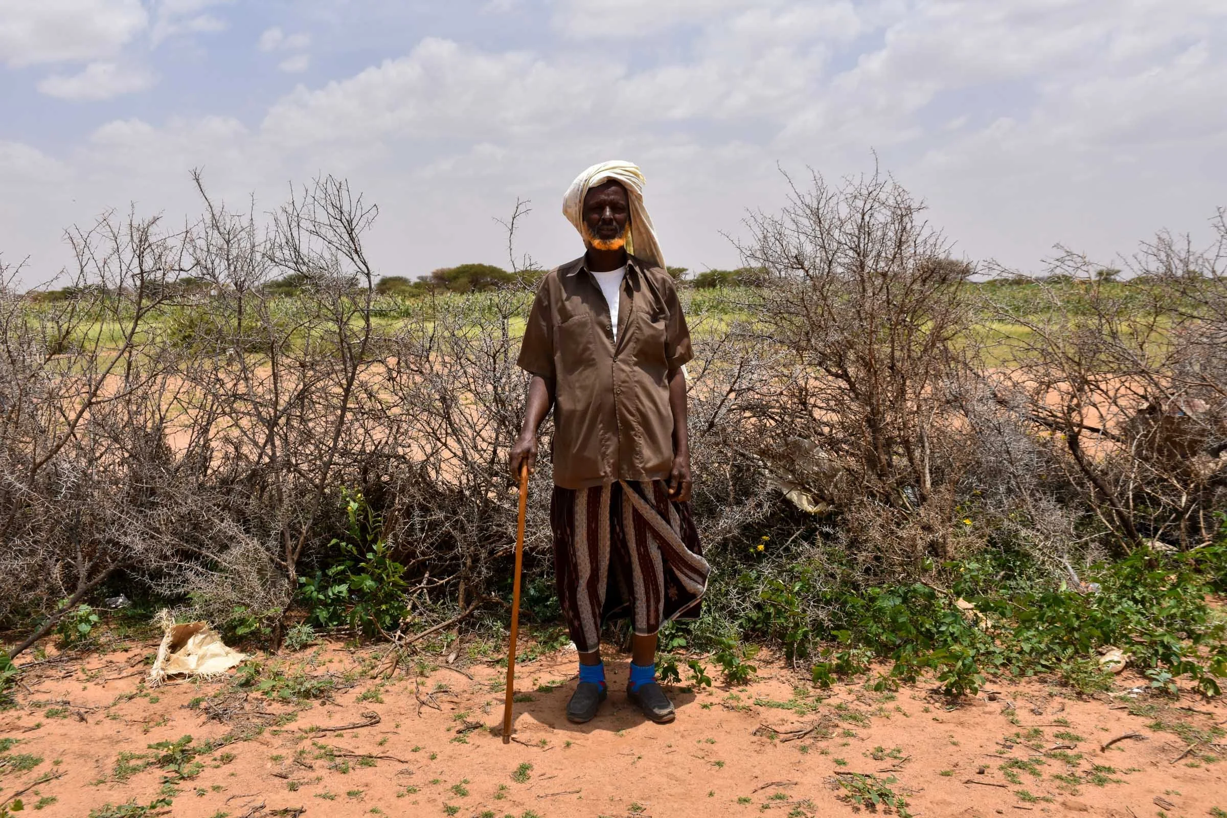 A man stands for a portrait in front of a field while leaning on a stick