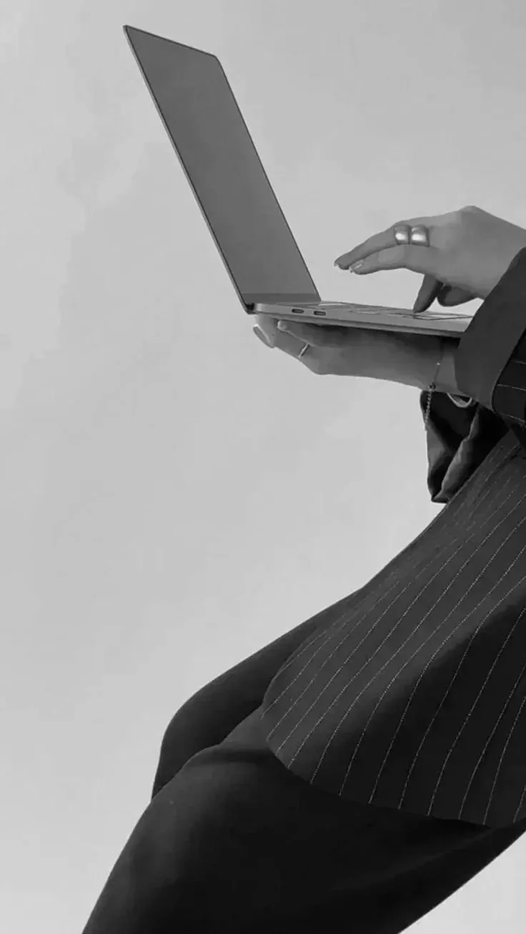 Una persona indossa un abito a righe e tiene un laptop aperto in mano, mentre usa un pennino o un mouse con la stessa mano.