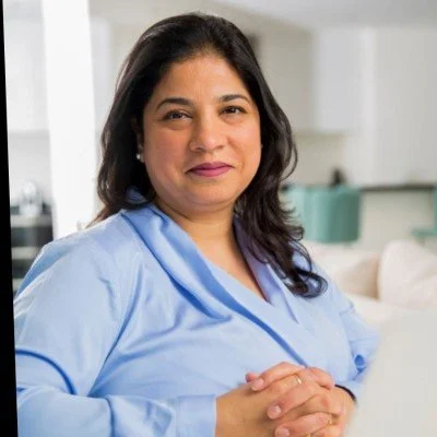 A woman in a light blue uniform sits at a desk in a medical or professional setting, smiling at the camera.