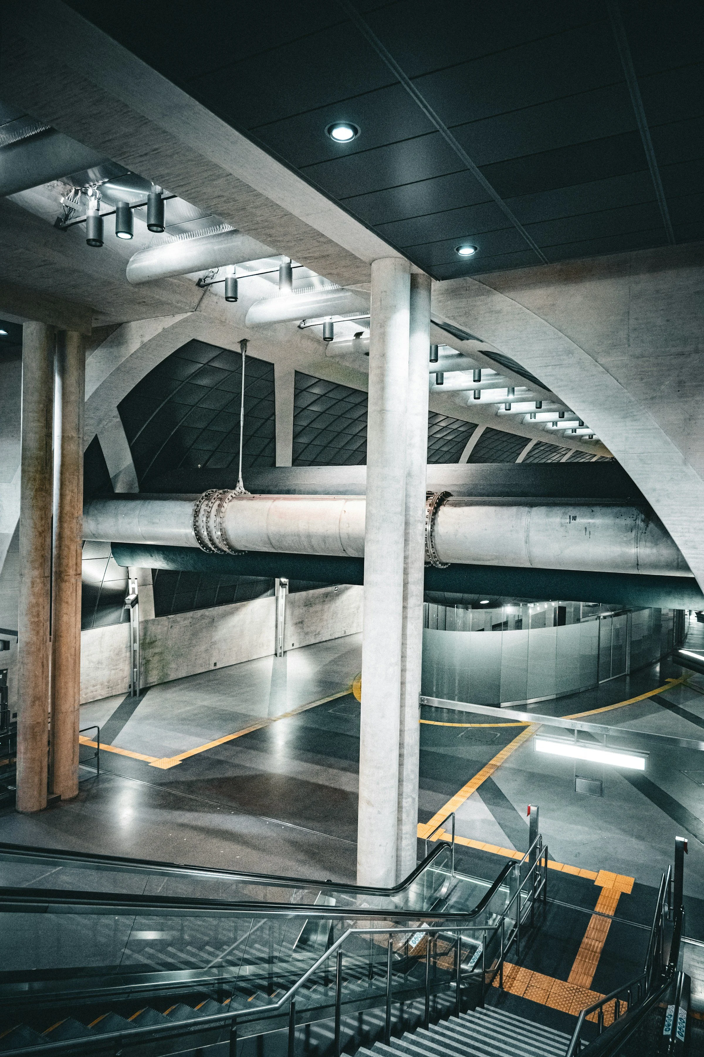 An empty underground parking garage with concrete columns, ductwork, and modern lighting, along with a staircase and glass barriers.