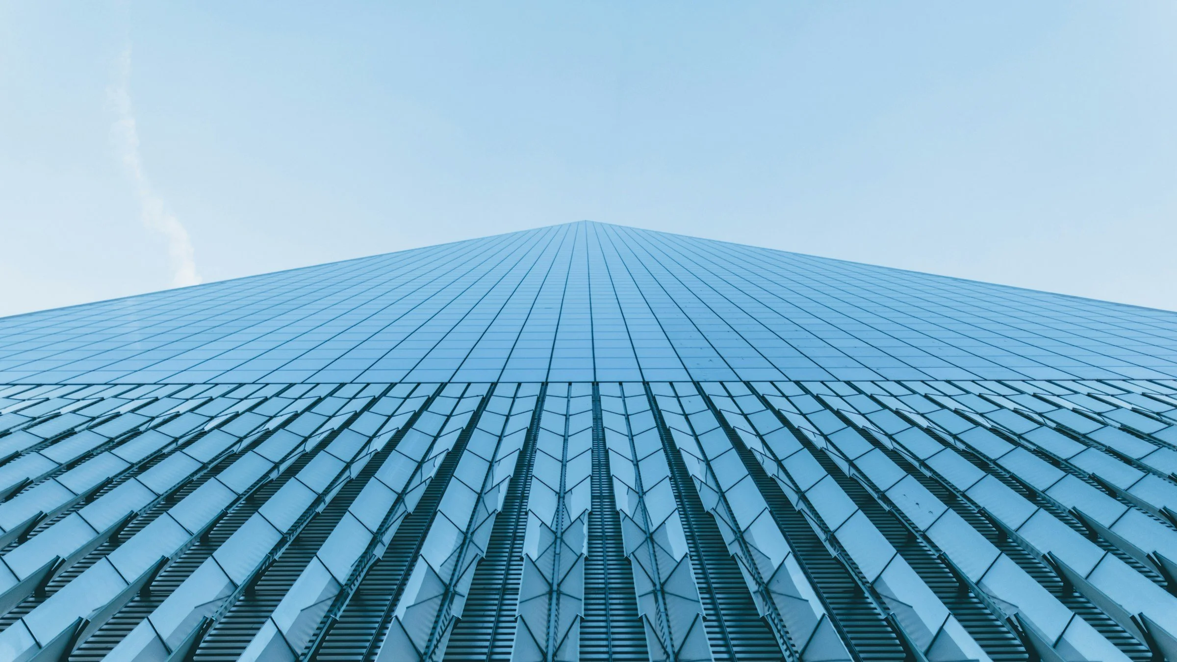 View upward of a tall, modern glass skyscraper reflecting the sky, with a blue sky background.