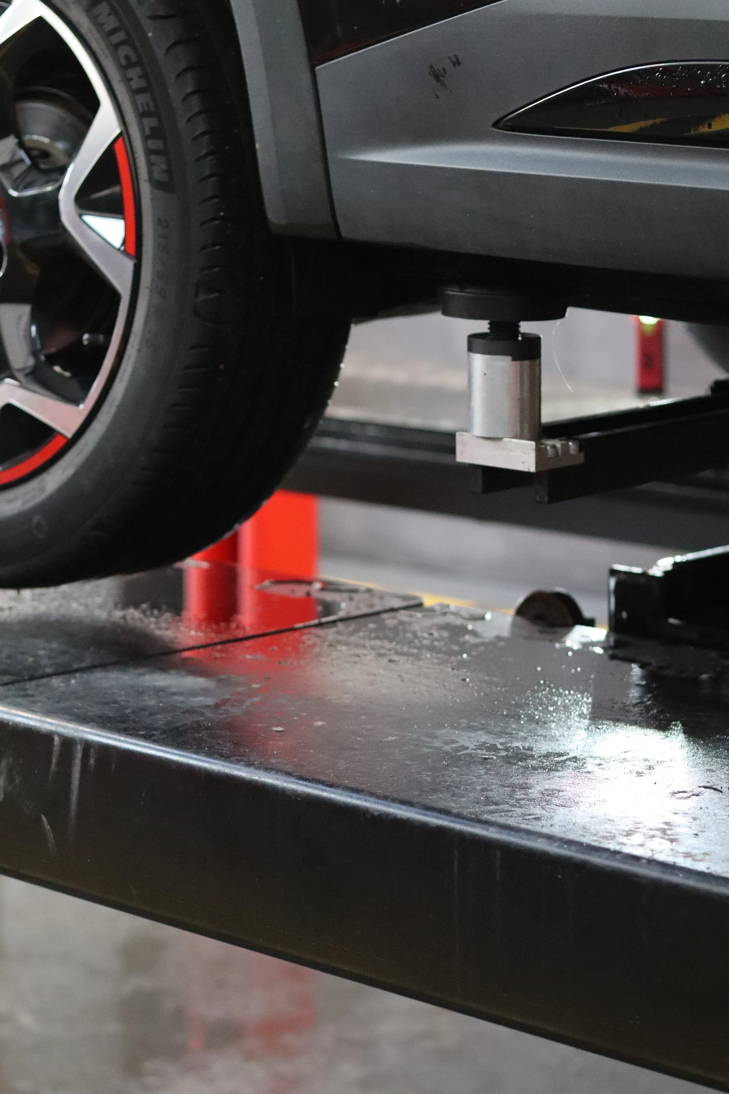 A car on a lift in a garage, with the rear wheel visible and a hydraulic lift underneath.