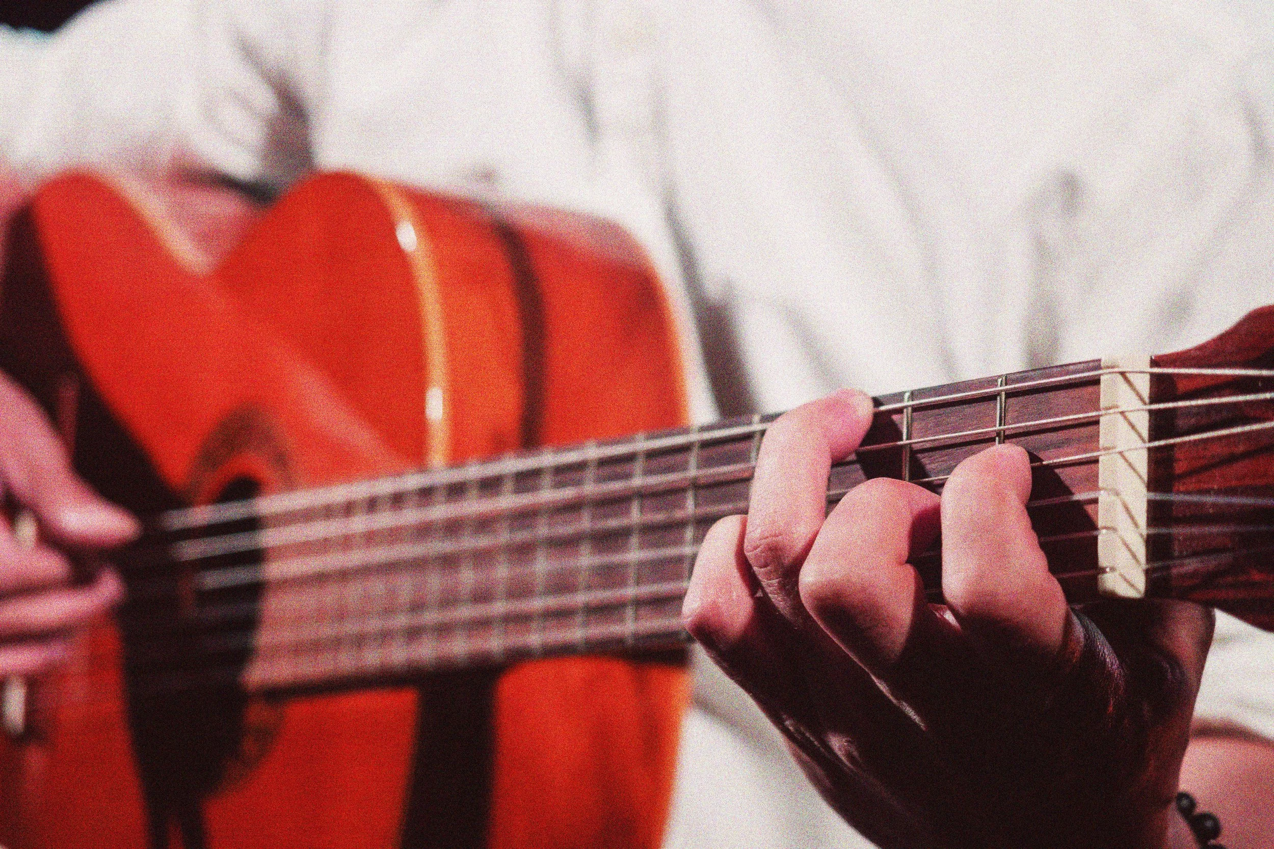 Persona tocando una guitarra acústica, enfoque en sus manos y en el cuerpo de la guitarra de color anaranjado.