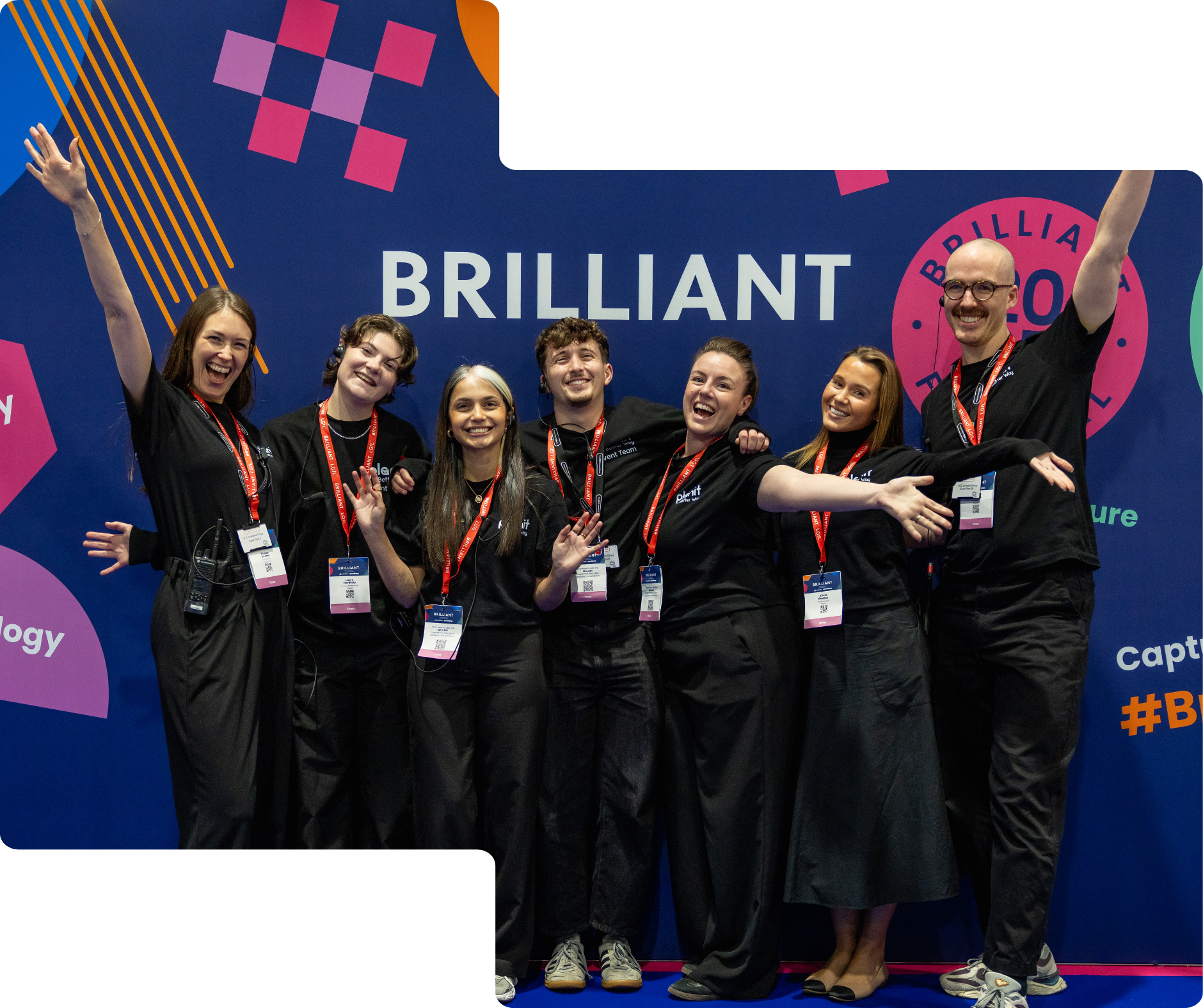 Group of seven smiling young people, wearing black shirts with red lanyards, standing together on stage at a conference, with a blue backdrop that reads 'BRILLIANT' and colorful geometric designs.