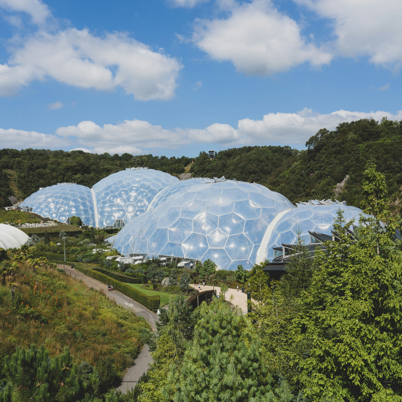 Glass domes set amidst greenery, with a clear blue sky and white clouds overhead.