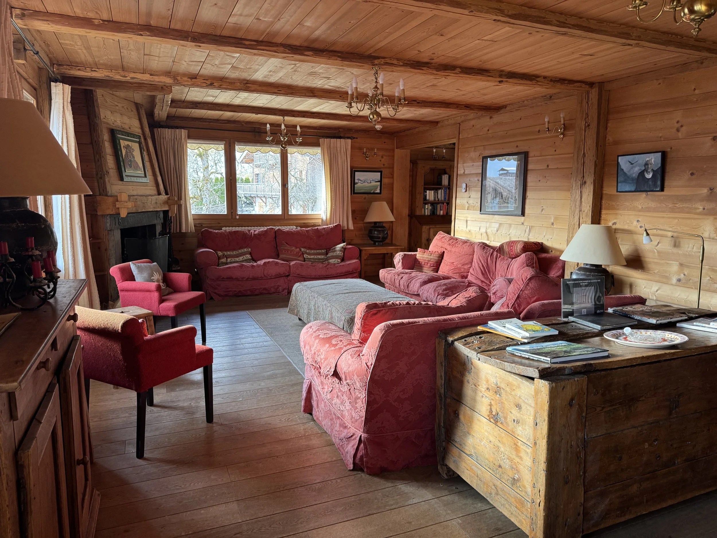 Cozy living room with wooden walls and ceiling, red sofas, a fireplace, a coffee table, and various decorative items.