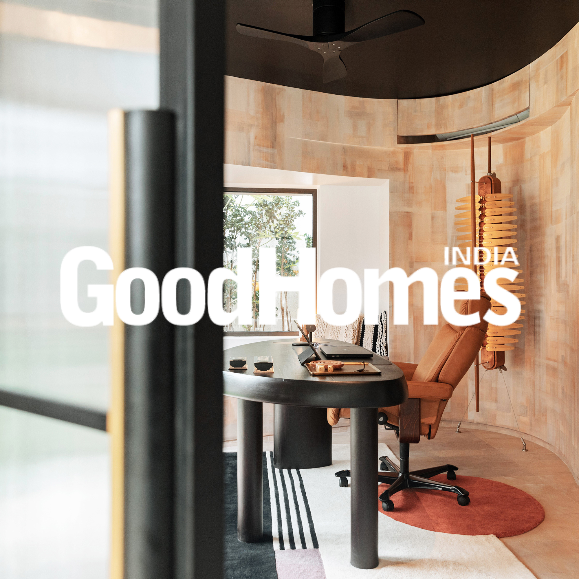 Modern office with curved wooden wall, black ceiling fan, orange office chair, and unique floor lamp, with table, laptops, and a window showing greenery outside.
