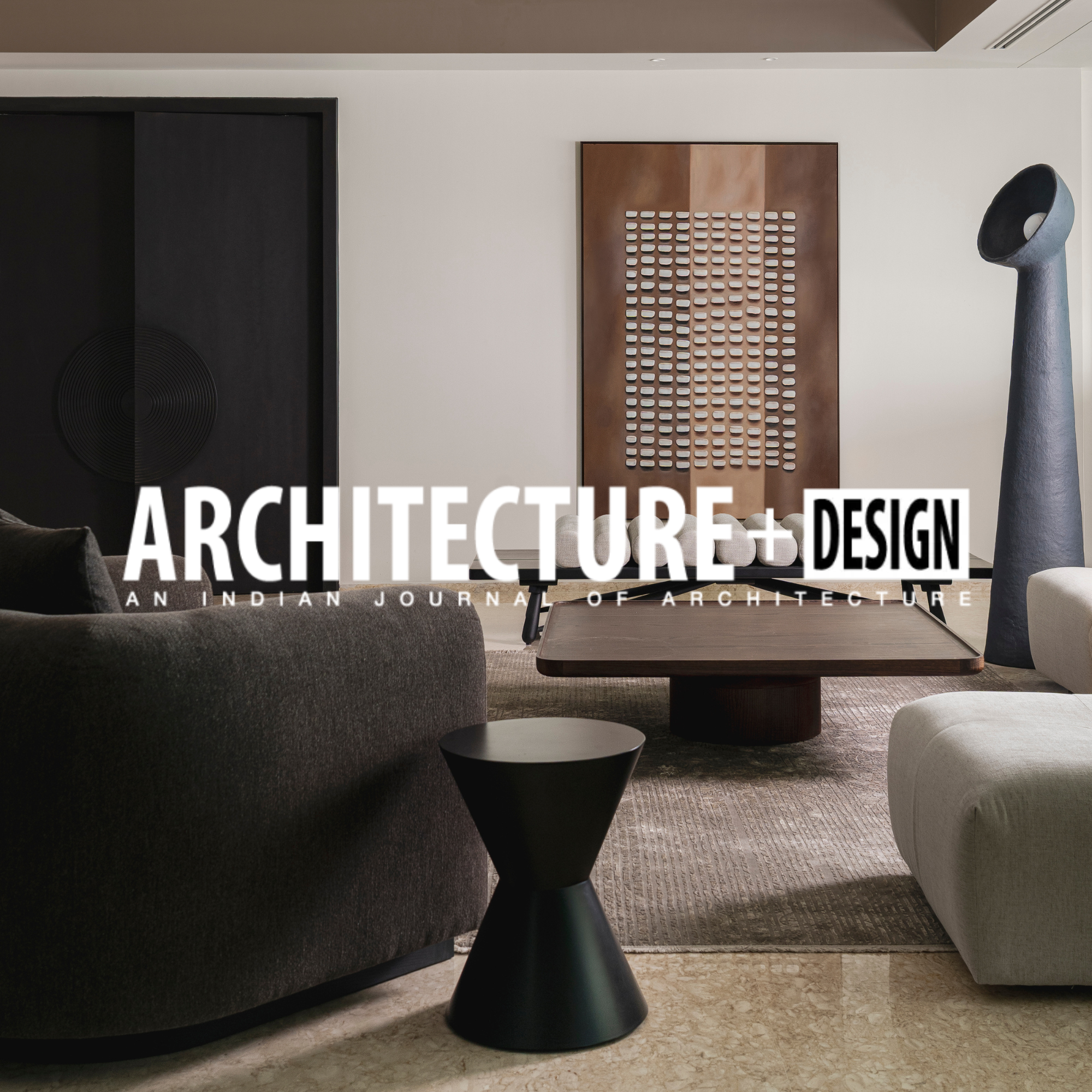 Modern living room with dark brown and light gray sofas, wooden coffee table, and decorative sculptures, with the text "ARCHITECTURE + DESIGN" overlayed on the image.