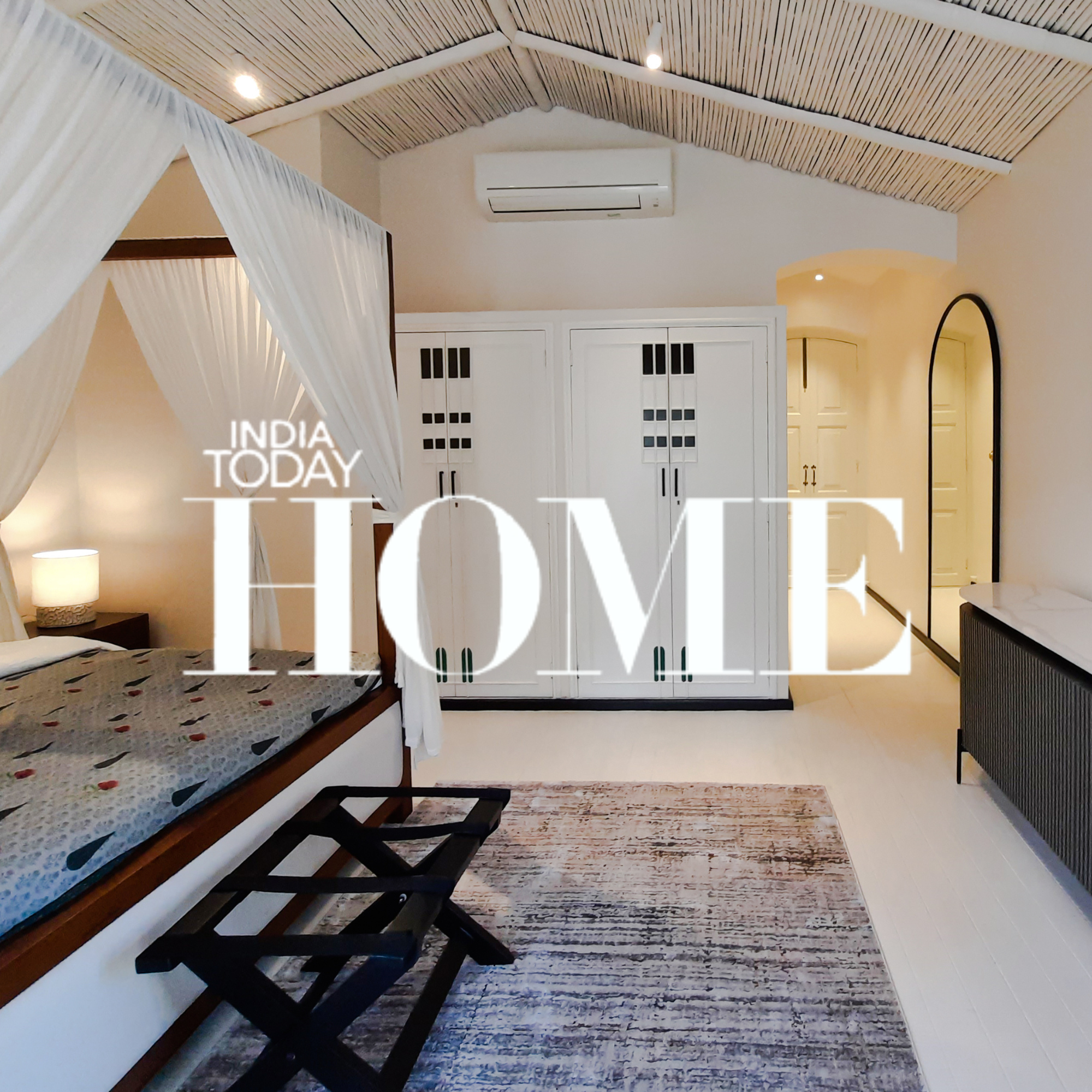A modern bedroom with a four-poster bed, a black bench at the foot, white wardrobes, a dresser, a mirror, a rug, and ceiling air conditioning, with a minimalist and cozy aesthetic.