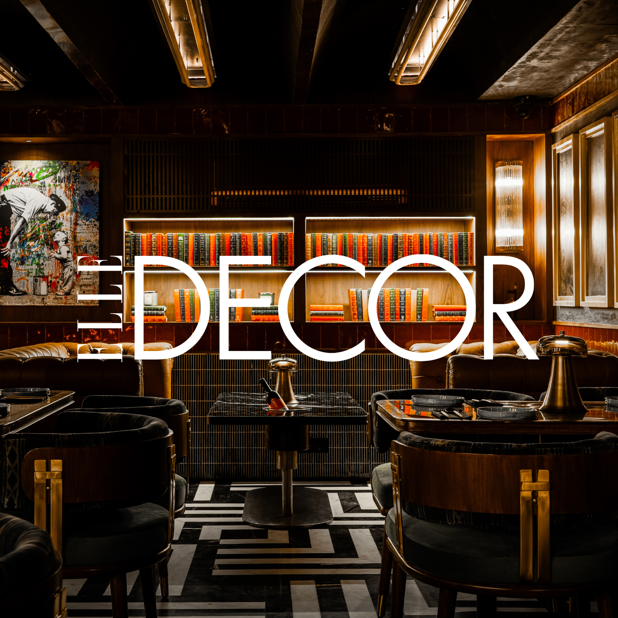 A dimly lit modern bar or lounge with black and gold furniture, a bookshelf with colorful books on a wooden wall, and a large picture of a mural or graffiti art on the left. The word 'DECOR' is overlaid on the image.