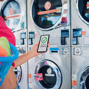 Person using a smartphone to make a payment at a laundromat with coin-operated washing machines.