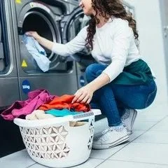 Woman loading laundry into a washing machine with a basket of clothes nearby.