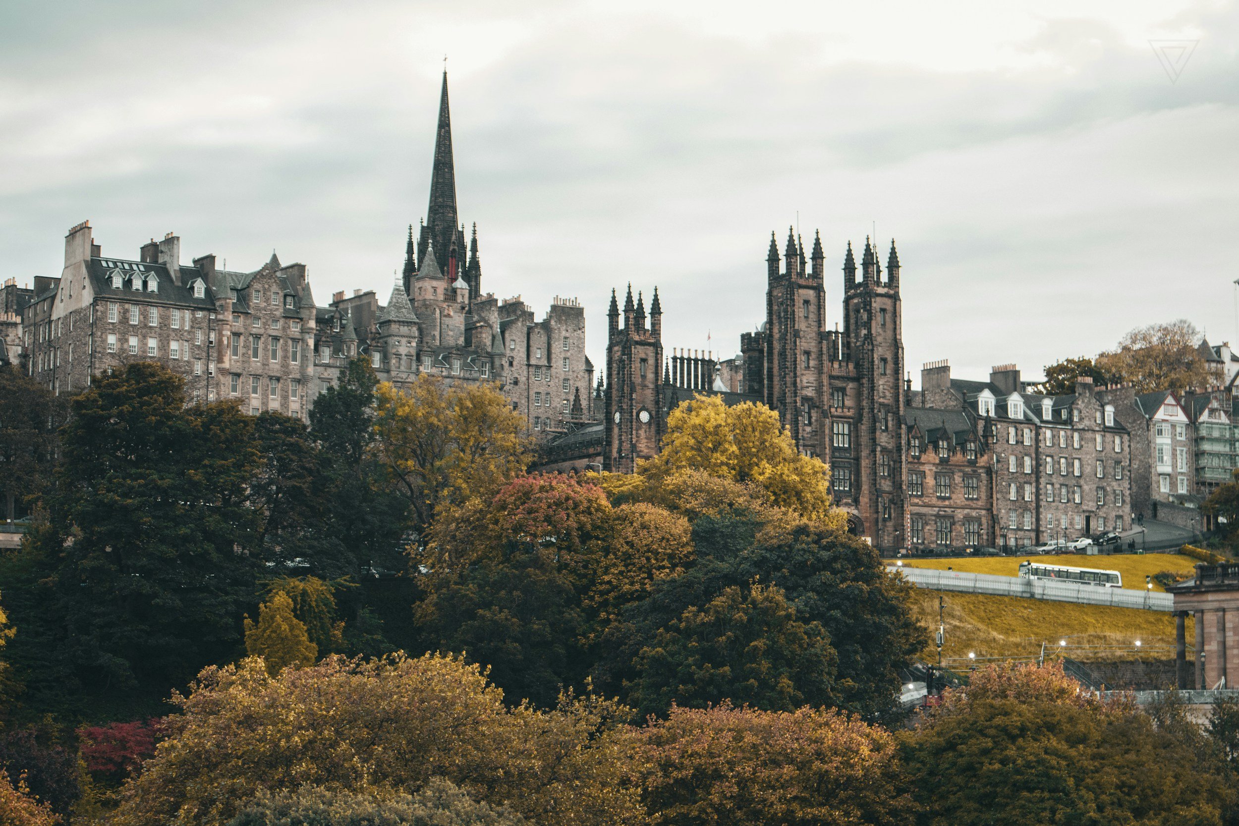 A cityscape featuring historic buildings and a church with a tall spire, surrounded by fall-colored trees on a cloudy day.