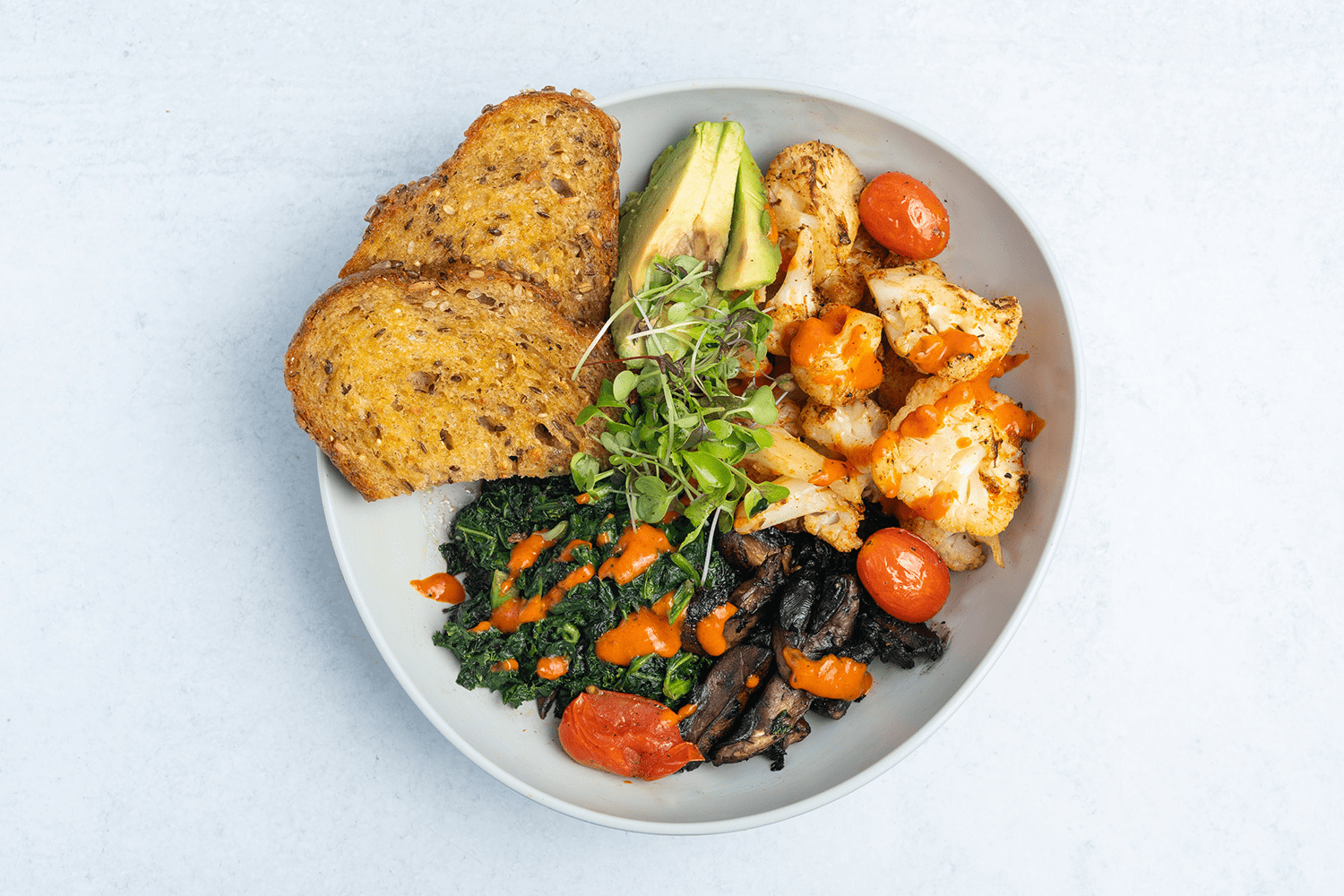 Bowl with toast, shrimp, greens, mushrooms, and tomatoes.