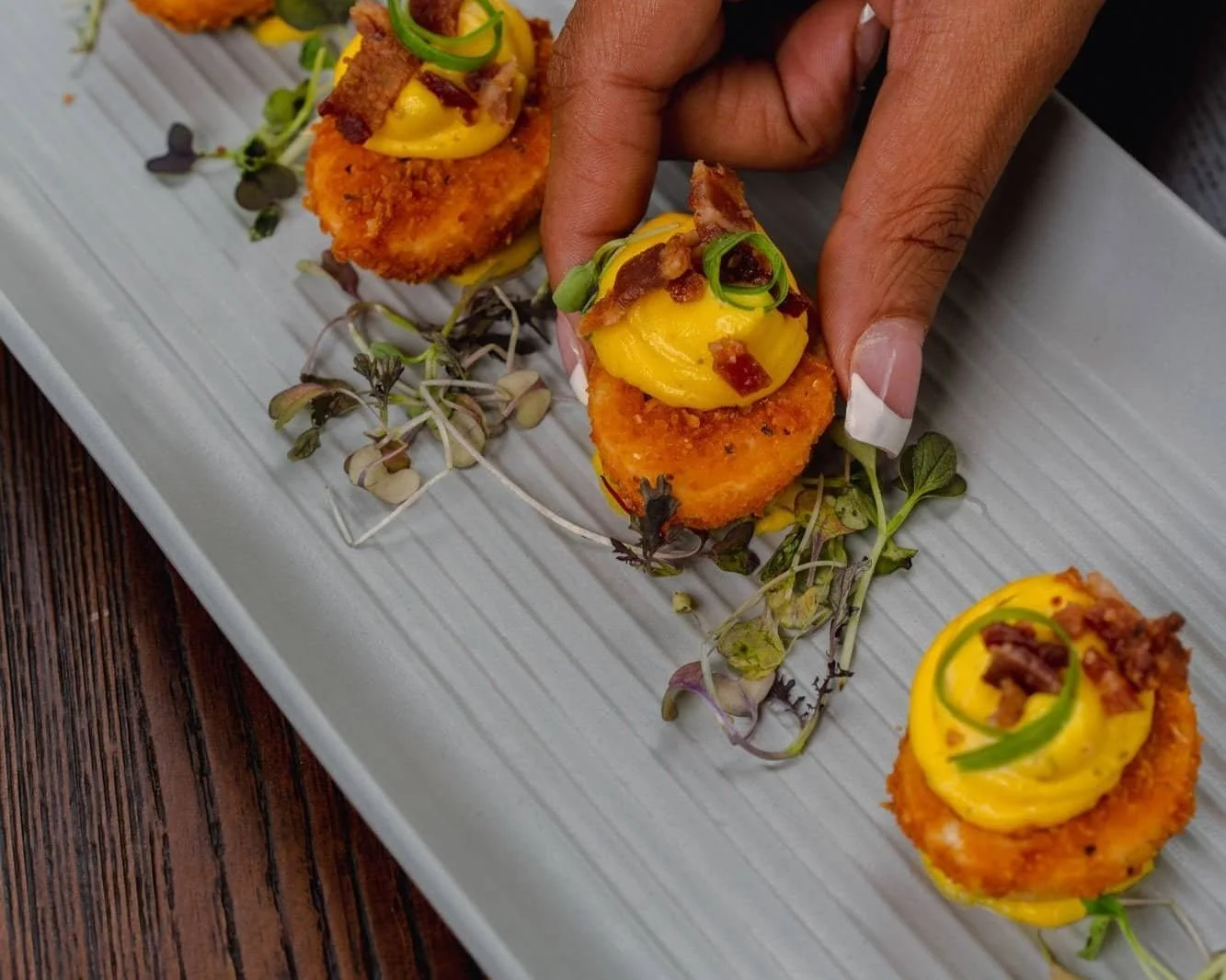 Crispy rounds topped with creamy deviled egg filling, bacon crumbles, and fresh herbs, served on a rectangular platter.