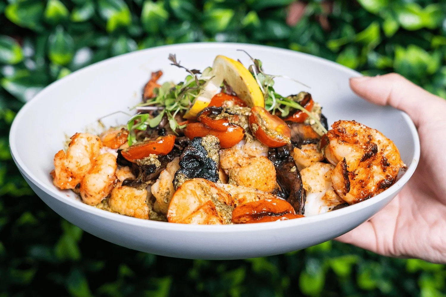 Bowl of grilled shrimp and vegetables with lemon garnish.