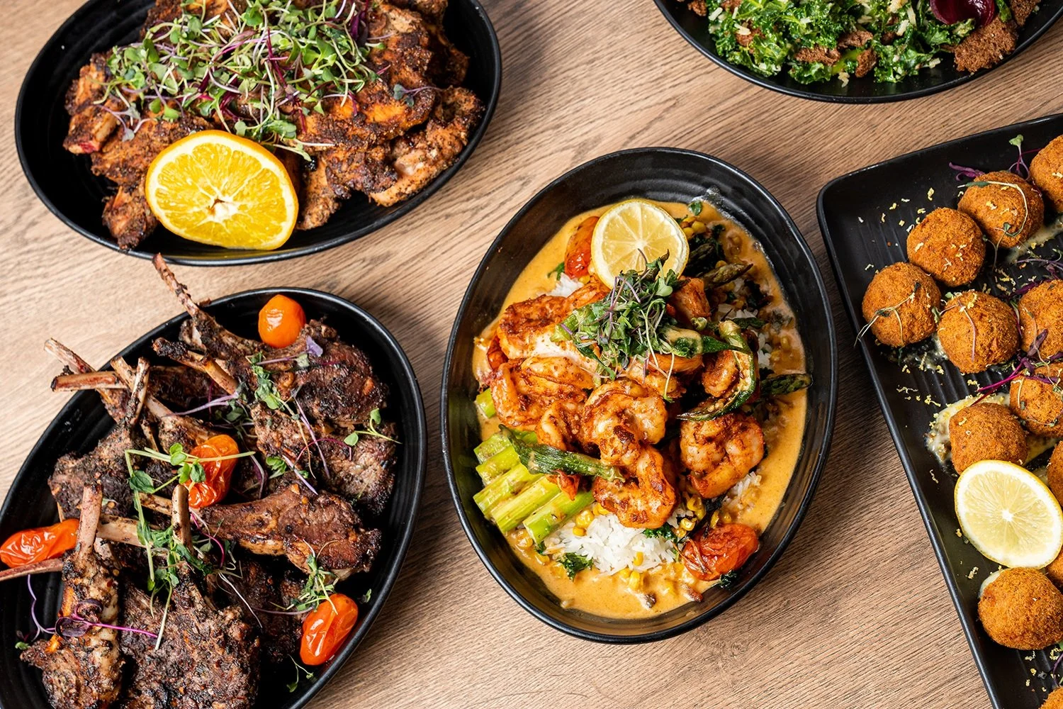 Assorted Southern dishes with lamb chops, shrimp in sauce, salad, and hush puppies.