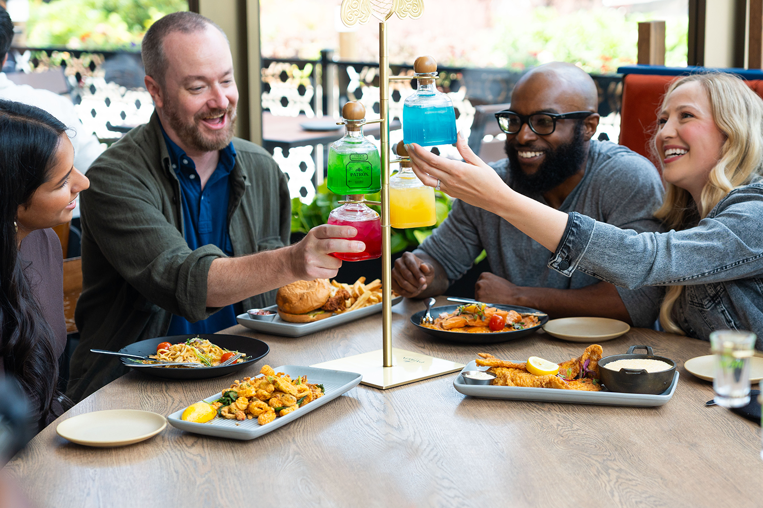Group of friends enjoying a meal together and raising colorful cocktails in a toast at a restaurant table.