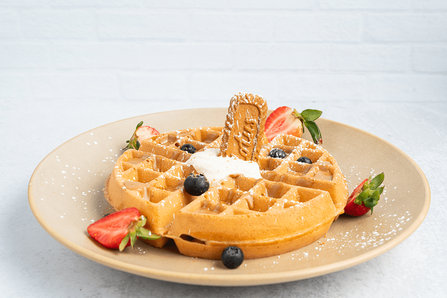 Southern-style chicken and waffles topped with fresh strawberries, powdered sugar, and a cookie garnish.