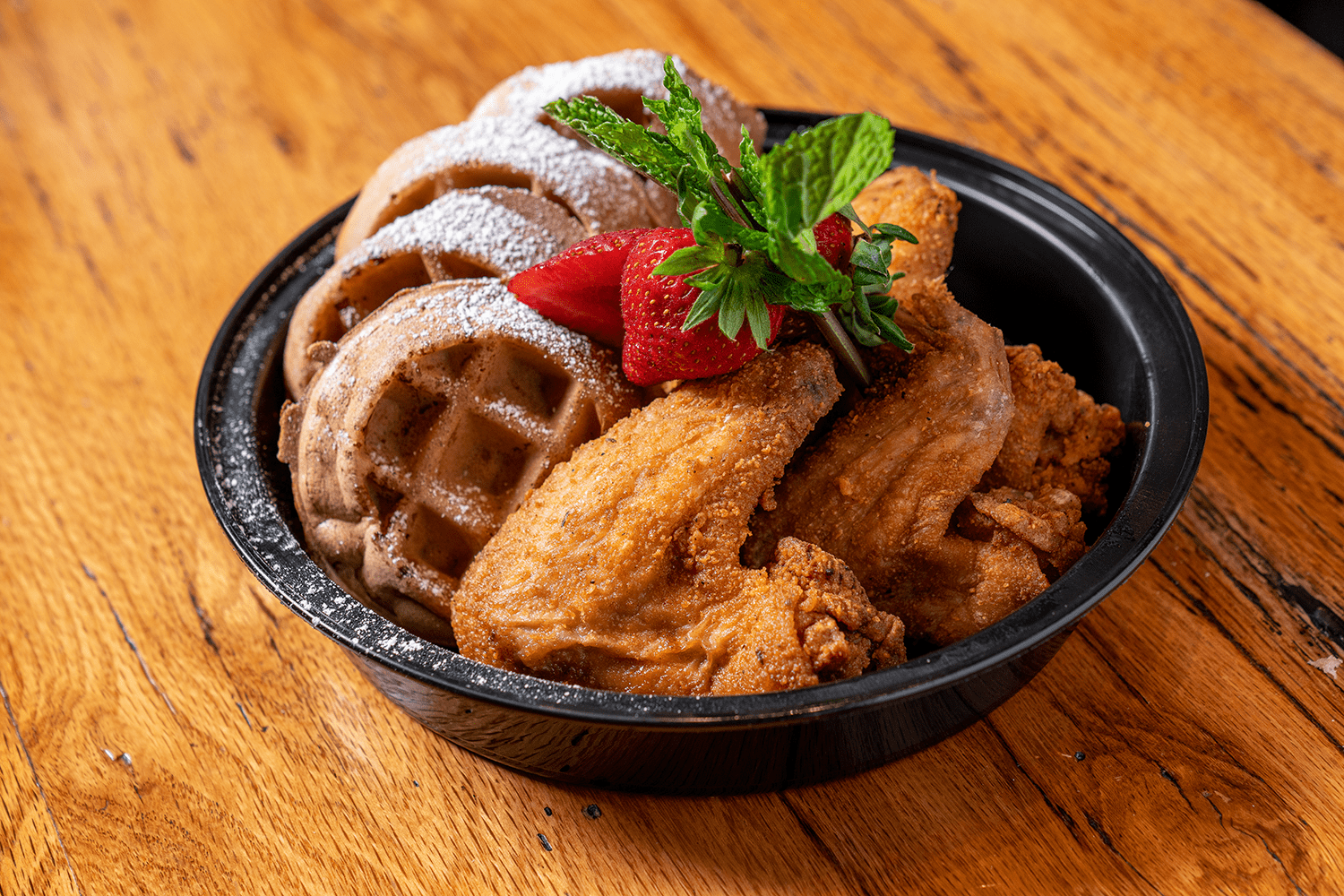 Fried chicken with waffles, powdered sugar, and strawberries.
