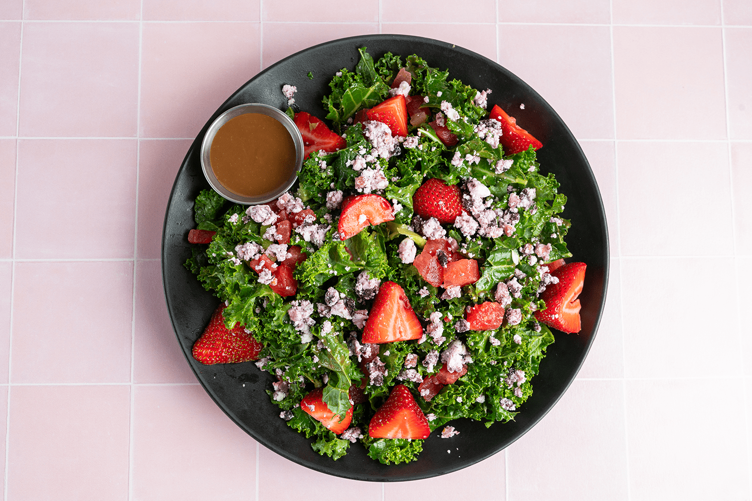 Fresh kale salad topped with sliced strawberries, crumbled cheese, and served with a side of vinaigrette dressing.