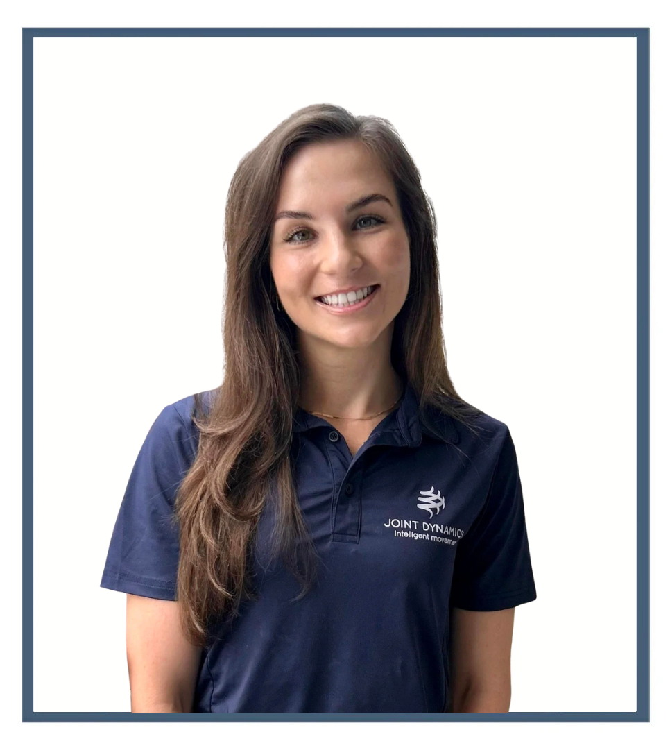 Young woman with long brown hair smiling on a balcony in an urban cityscape, wearing a navy polo shirt with a logo.