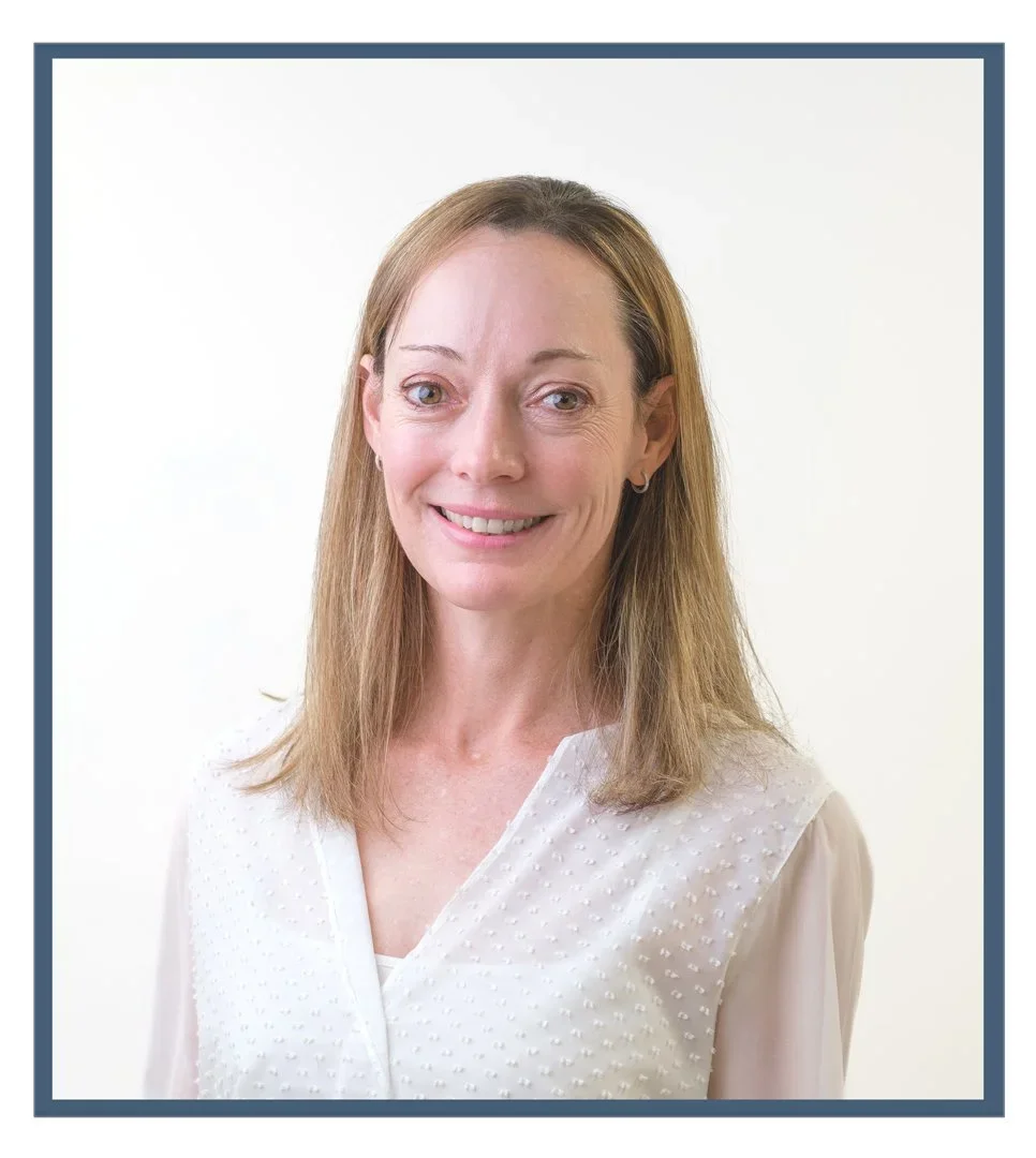 A woman with long brown hair wearing a black shirt with a logo and the words 'Joint Dynamics' printed on it, standing against a white background.