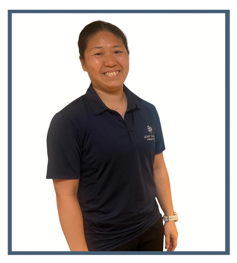 A woman smiling while sitting on a boat, wearing a wetsuit and holding a snorkel, with water and mountains in the background.