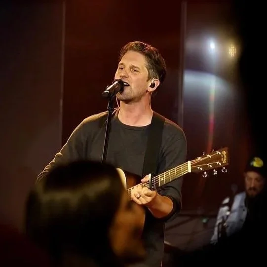 Un homme chante et joue de la guitare enregistrement en studio, avec un micro, ambiance chaleureuse et musicale.