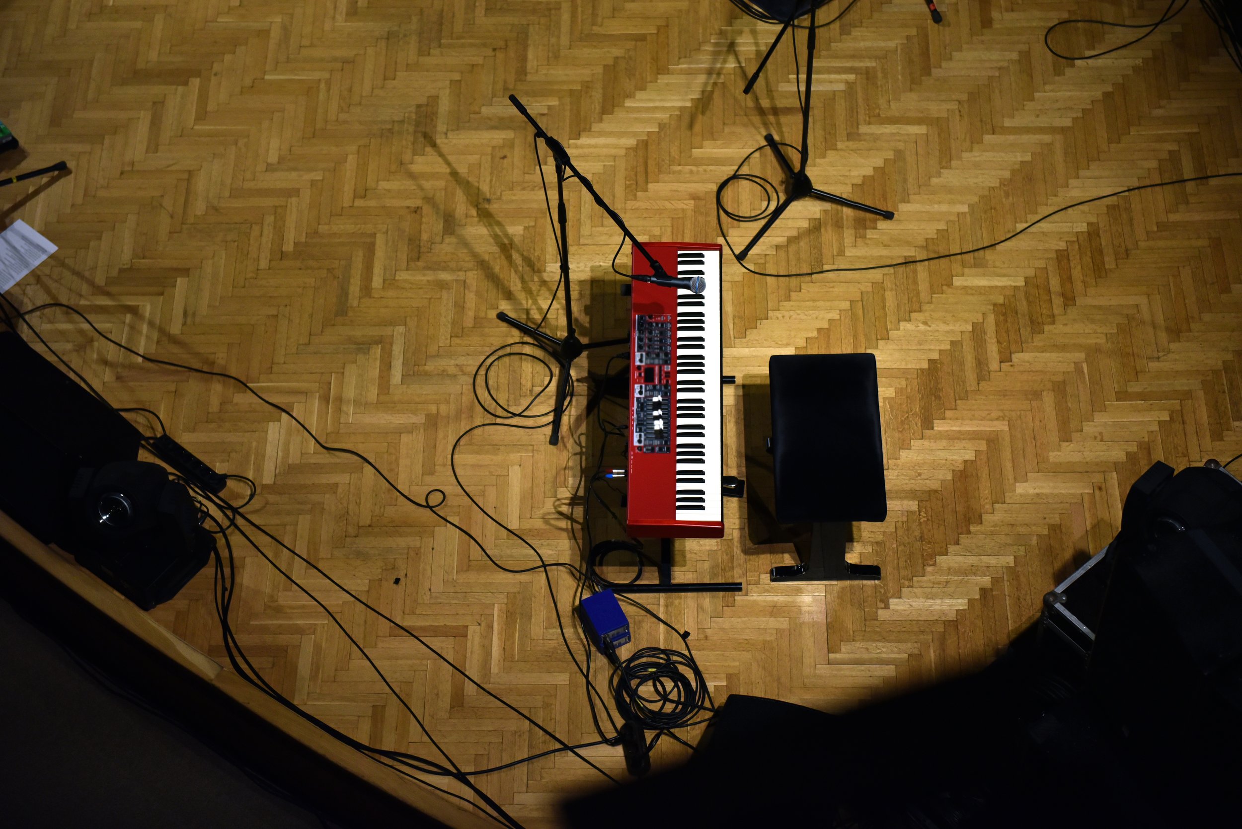 Scène d'un enregistrement musical avec un clavier rouge, un tabouret noir, plusieurs micros et câbles posés sur un sol en parquet.