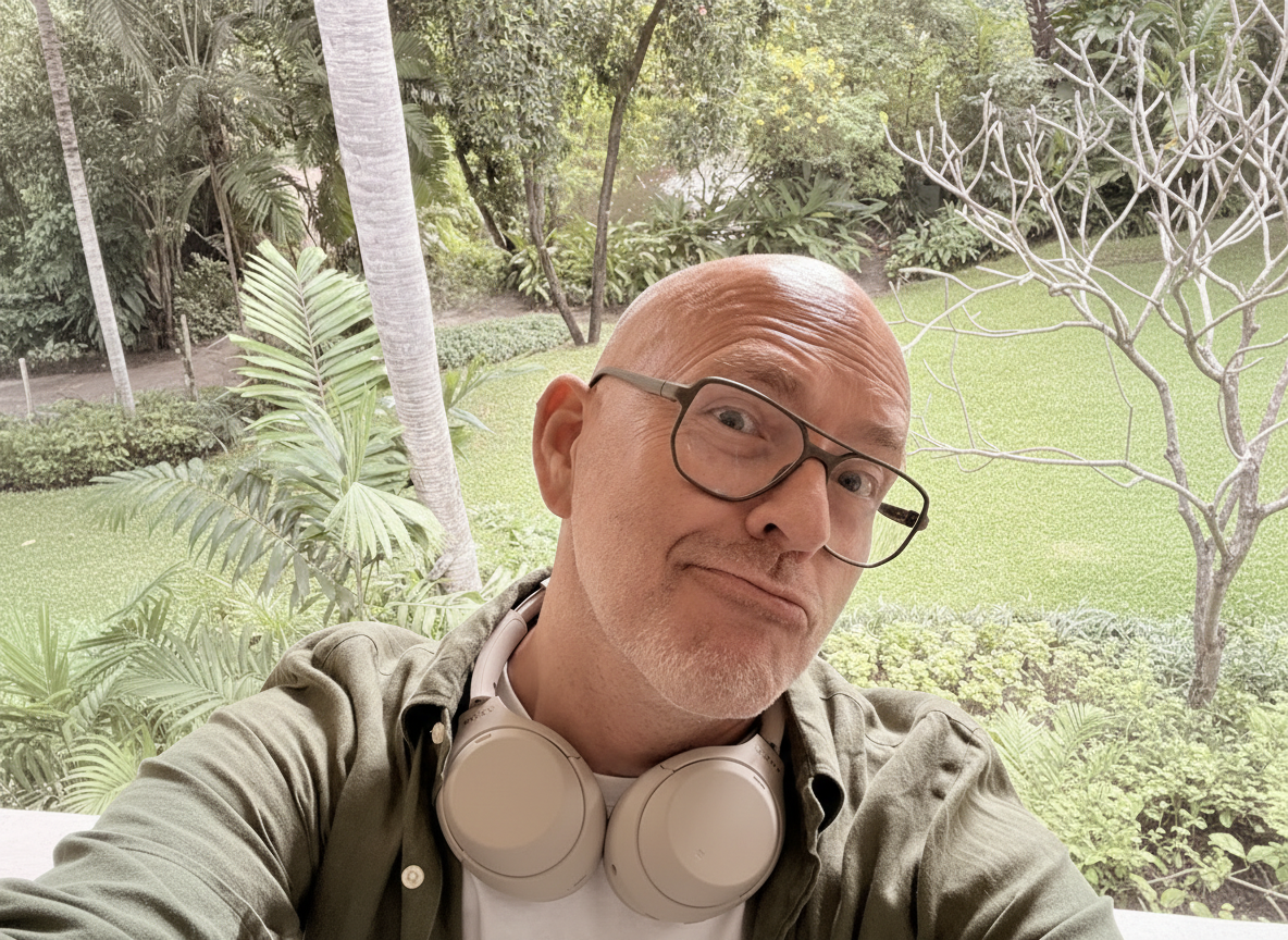 Mann mit Brille und Kopfhörern auf einem Balkon vor einer grünen Gartenlandschaft