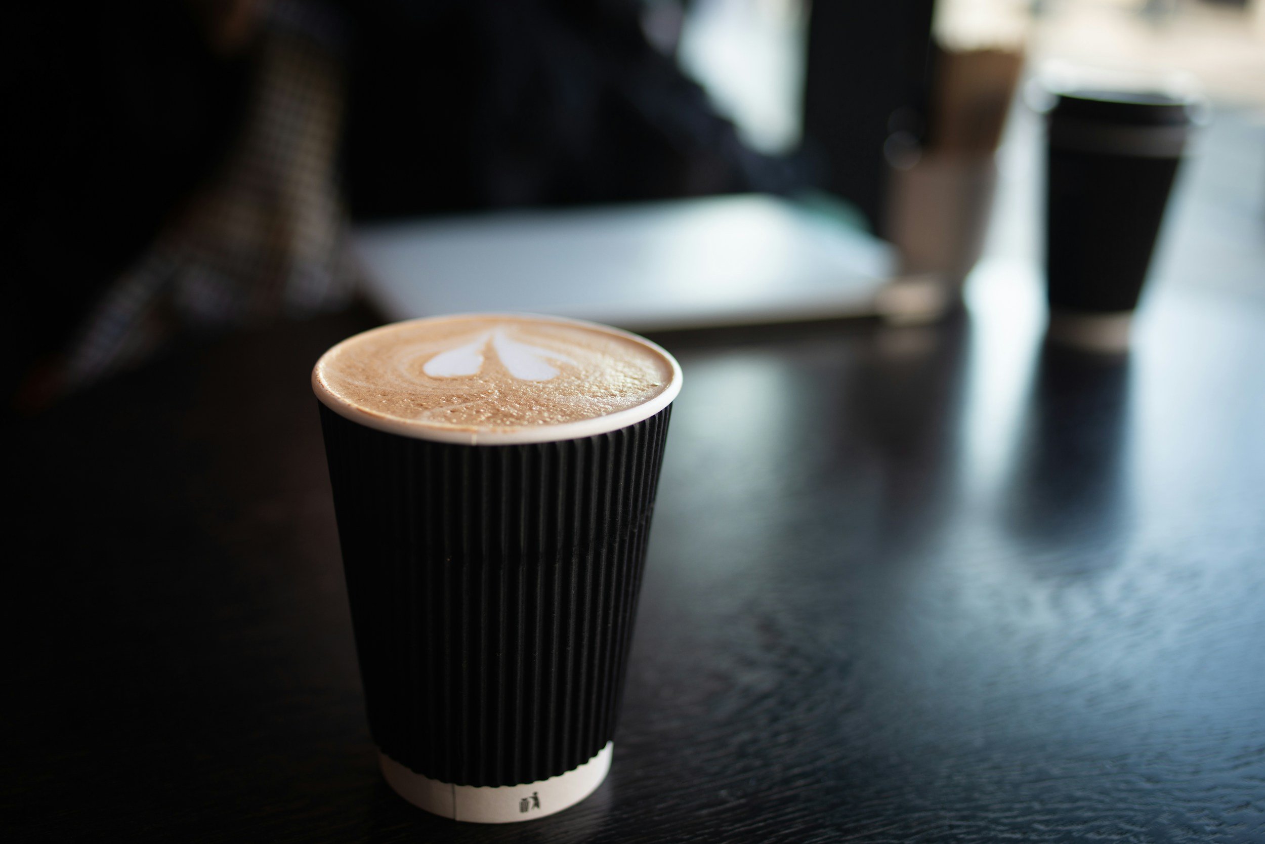 Een kop koffie met latte art op een zwarte tafel, omringd door koffiebekers en een koffiekop.