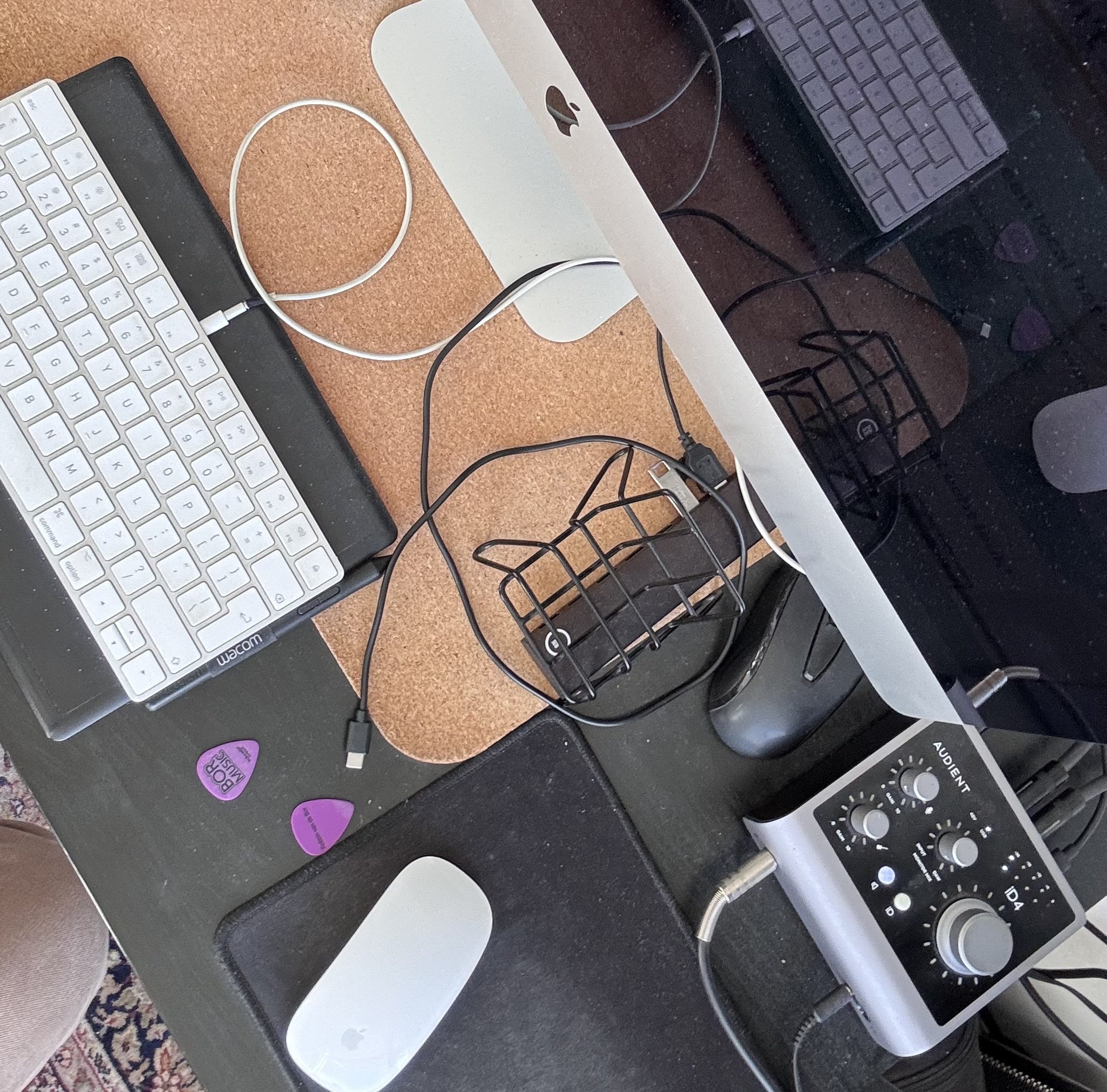 Computer desk with a white keyboard, a computer mouse, a small monitor, a monitor stand, various cables, a black desk organizer, a speaker with controls, and purple guitar pick-shaped items on the desk.